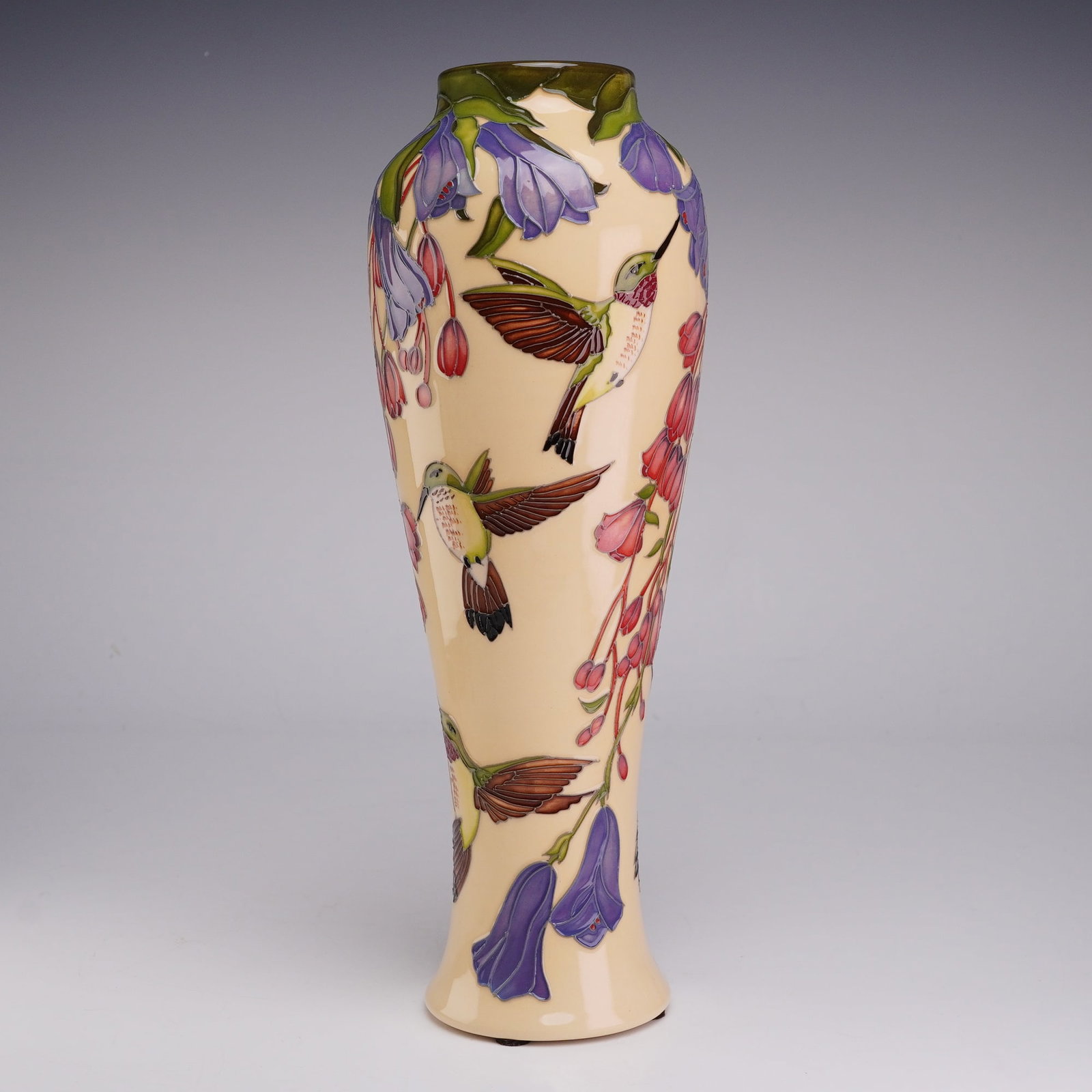 Moorcroft Pottery by Rachel Bishop Limited Edition Vase, Hummingbird: This Moorcroft art pottery vase features a tall, slender form with a flared base and a tapered neck. The piece is decorated using the tubelining technique, depicting hummingbirds in flight among trail