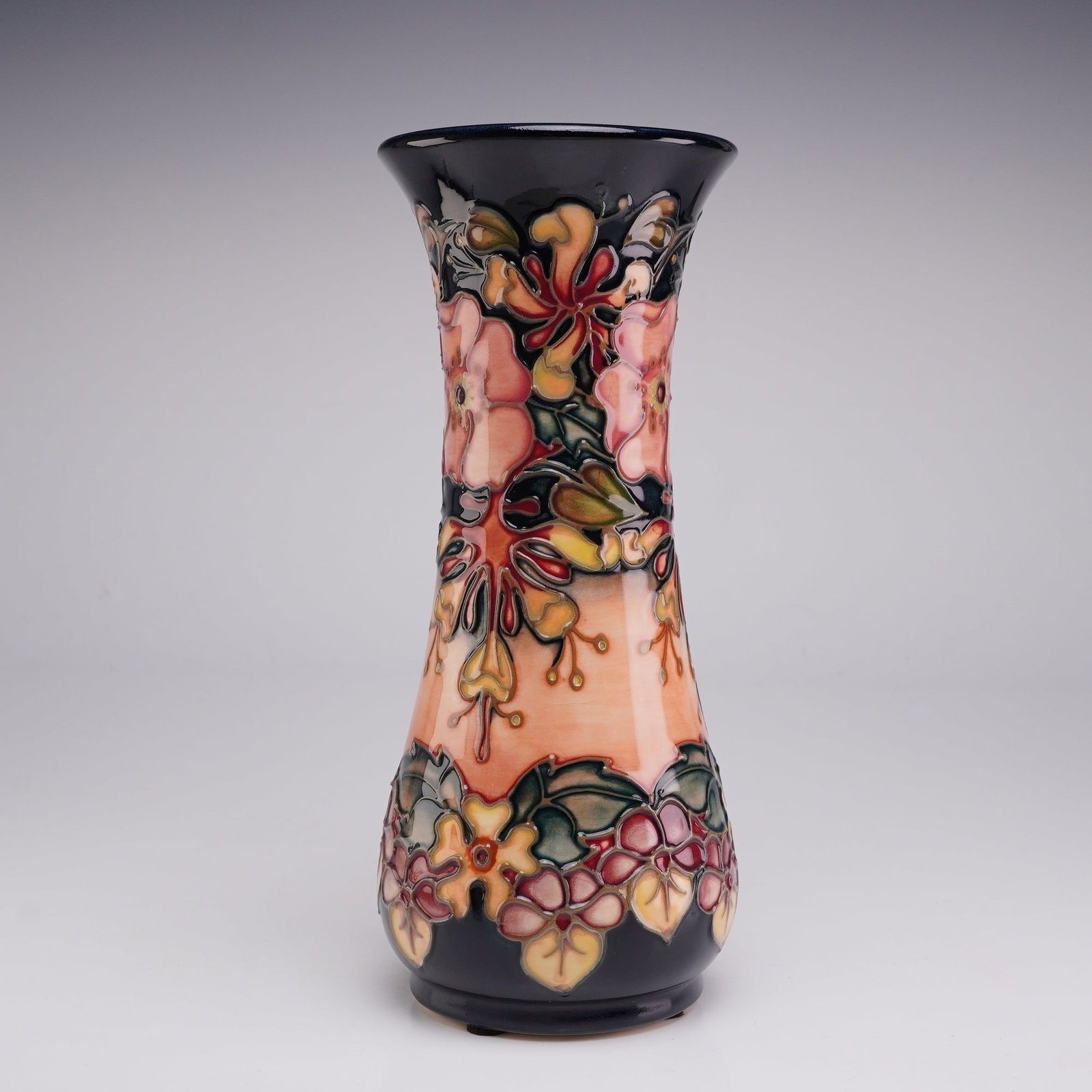 Moorcroft Pottery by Rachel Bishop Vase, Oberon: The vessel features a waisted silhouette with a flared rim and a bulbous base. The hand-painted tubelined decoration depicts a stylized Art Nouveau floral arrangement of pink, red, and yellow blossoms