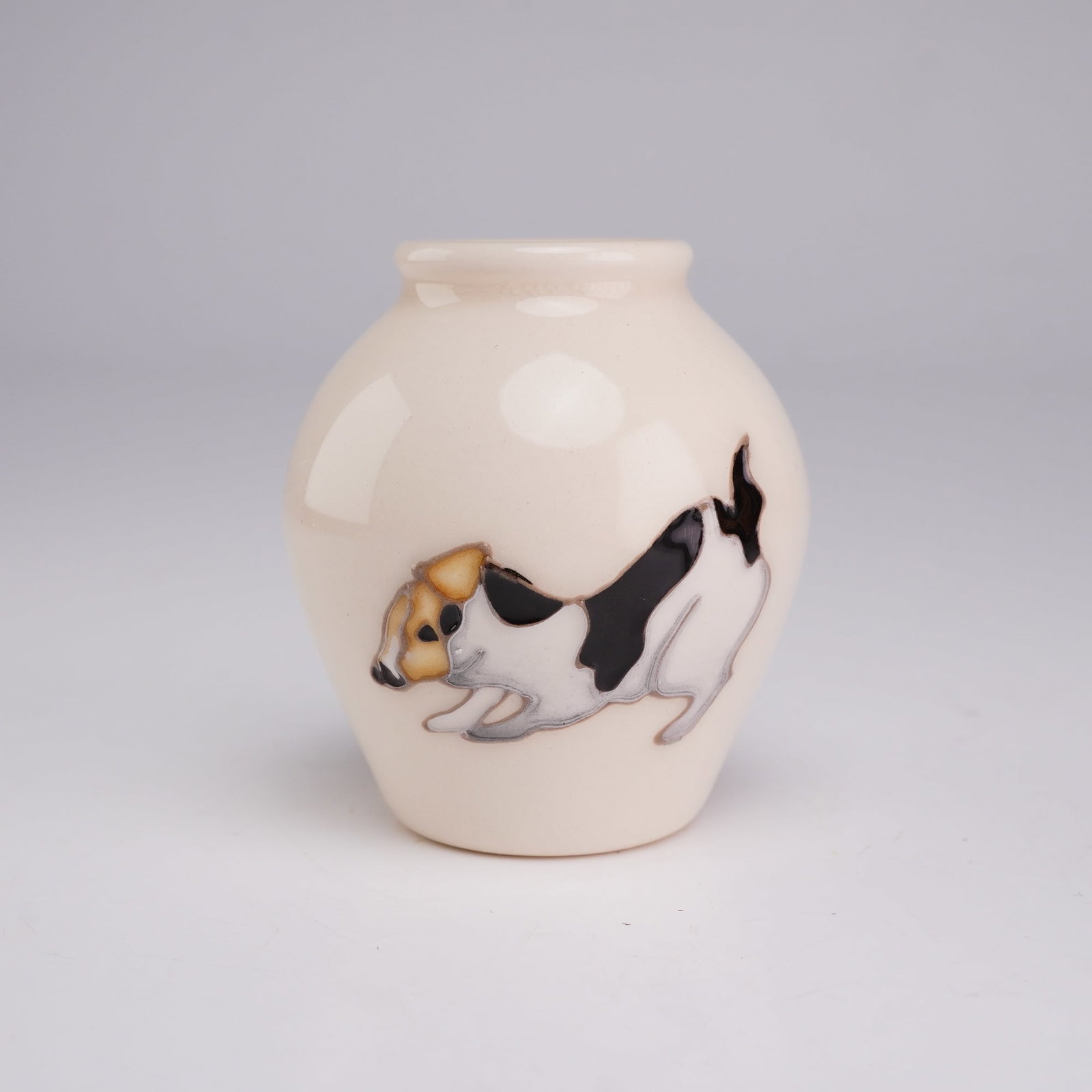 Moorcroft Pottery Miniature Dog Vase, Jack Russell Terrier: This miniature bulbous-form vase features a short neck and a flared rim, crafted from ceramic with a glossy cream-colored glaze. The exterior decoration consists of a hand-painted tricolor Jack Russel
