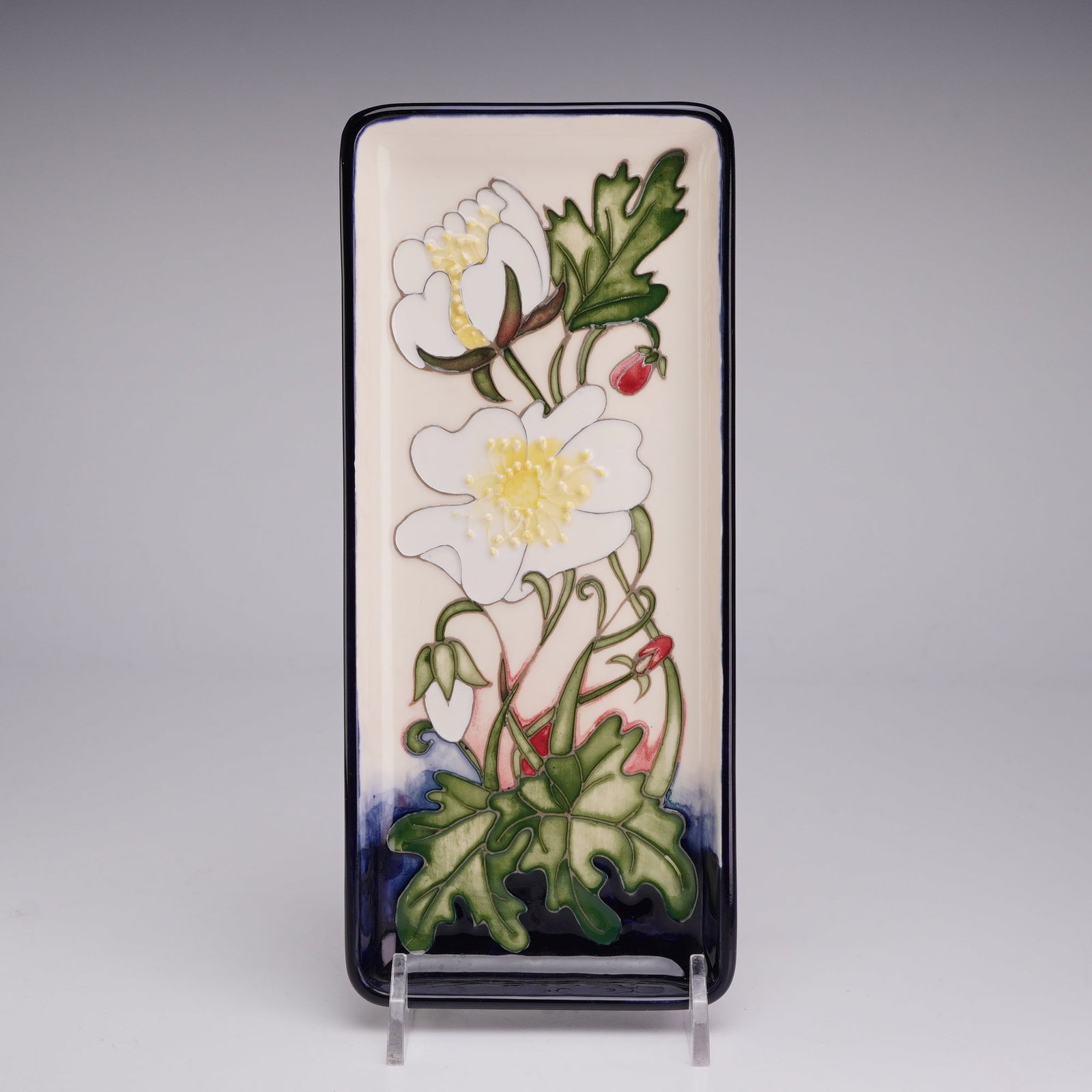 Moorcroft Pattern Trial Rectangular Pin Tray: The earthenware tray features a tube-lined design of white wild roses with yellow centers, accented by green leaves and red buds. The motif is set against a cream-colored ground that blends into a dee