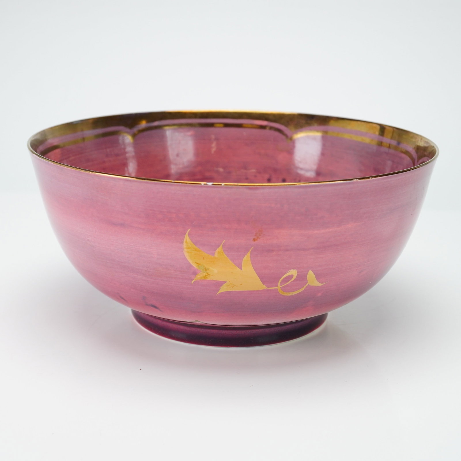 Wedgwood Ruby Lustre Porcelain Bowl with Gilt Leaf Decoration: This porcelain bowl features a deep circular form with a tapered body resting on a low, unglazed foot ring. The exterior is decorated with a variegated matte glaze in shades of dusty rose and mauve, s