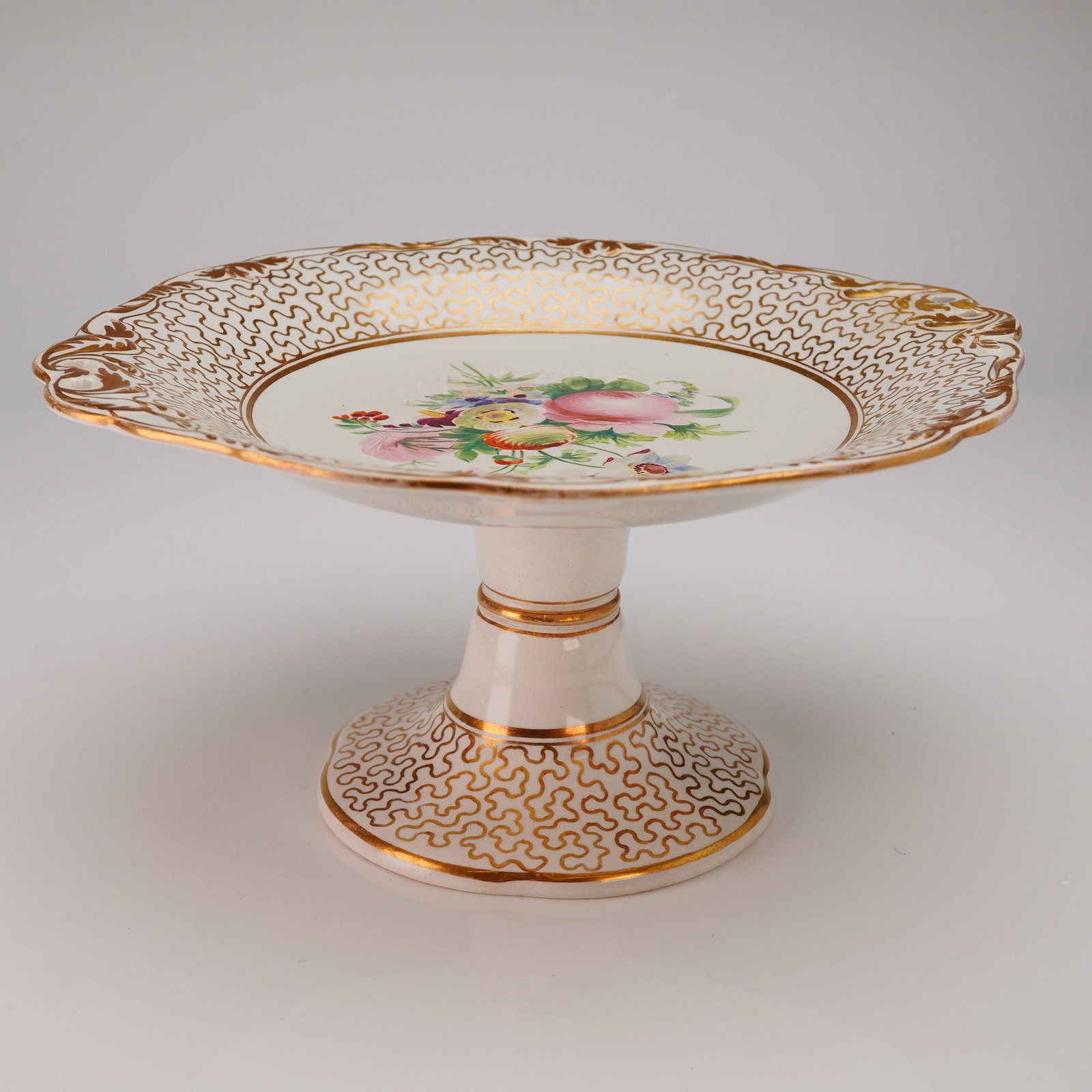 Wedgwood Pearl Gilt and Hand-Painted Ceramic Compote: A single ceramic pedestal serving piece. Featuring a broad, scalloped rim and a flared pedestal base. The decoration includes extensive gold (gilt) scrollwork covering the broad border and the flared 
