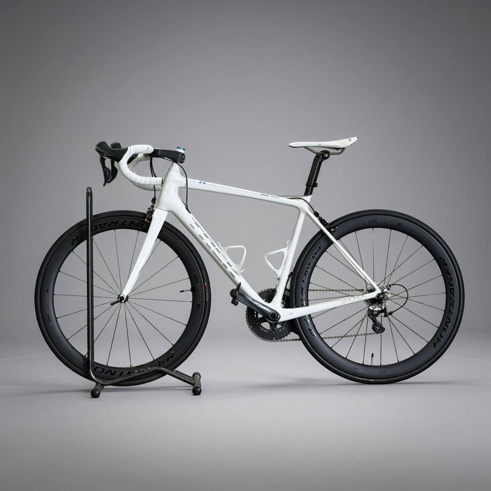 Trek Emonda SLR OCLV Carbon Road Bicycle with Shimano Ultegra Groupset and Willworx Superstand: A Trek Emonda SLR high-performance road bicycle featuring a frame and fork constructed from Trek OCLV Carbon fiber. The frame is finished in gloss white with silver-grey Trek branding and blue accents