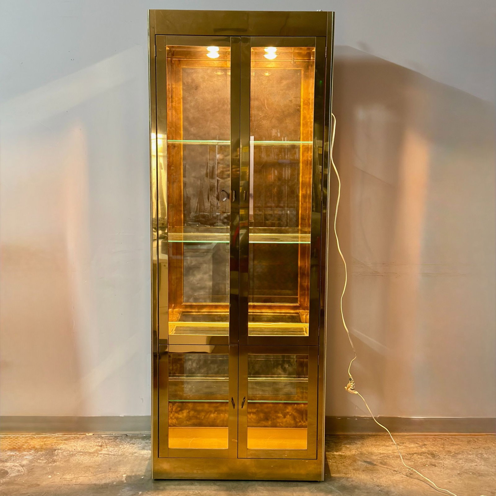 Large Hollywood Regency Polished Brass and Glass Vitrine Display Cabinet: A large Mastercraft vitrine display cabinet in the Hollywood Regency style featuring a polished brass-finished metal frame in a golden color. This one-piece unit is designed with two sets of double gl