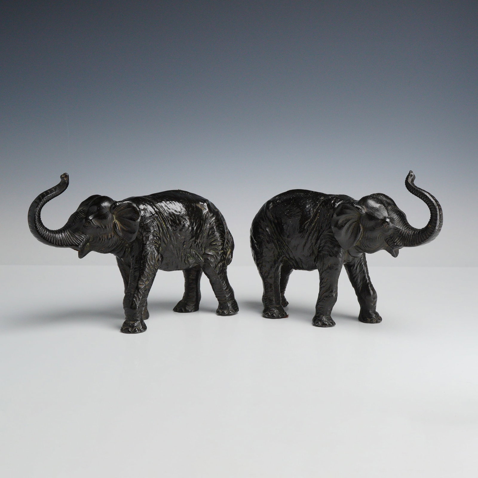 2pc Cast Metal Elephant Figurines with Raised Trunks: This lot of 2 metal elephants features cast metal figurines depicted in a walking pose with their trunks raised, a traditional symbol of good luck. The elephants are designed as a mirrored pair, with 