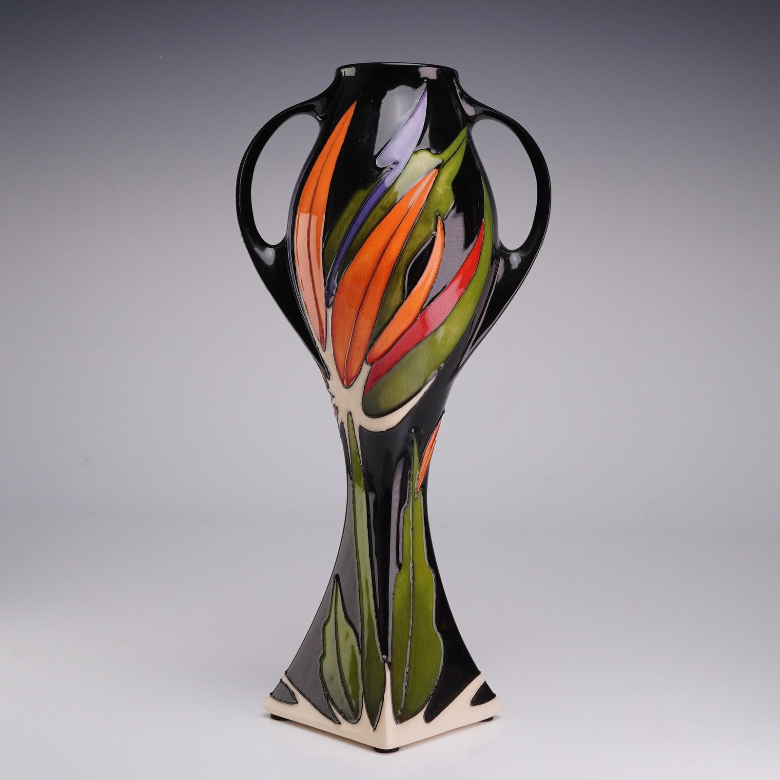 Moorcroft Pottery by Anji Davenport Two-Handled Vase, Paradise Found: The design is executed in a tube-lined Bird of Paradise floral motif, hand-painted with underglaze colors of orange, red, purple, and green set against a high-gloss black background. The form consists
