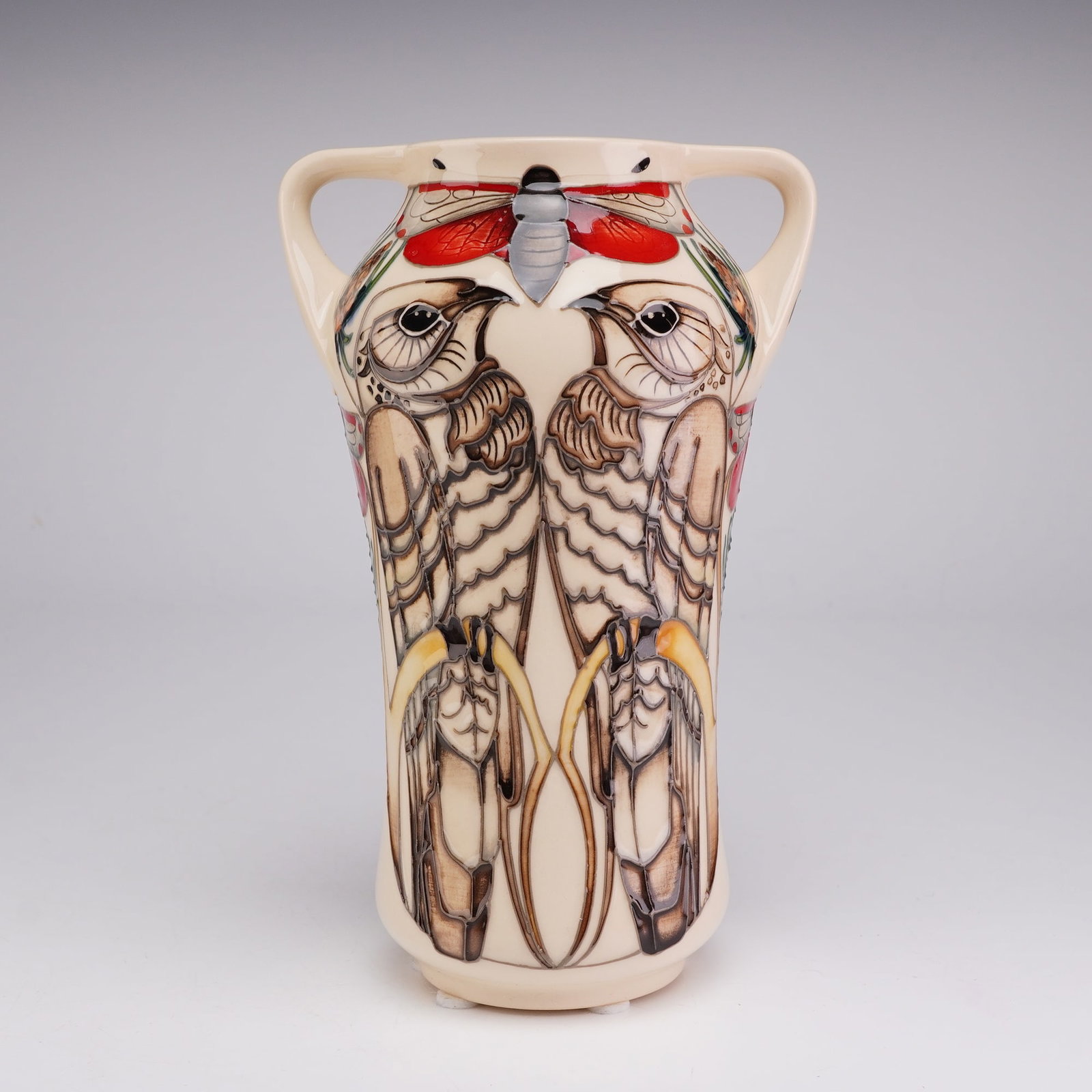 Moorcroft Pottery by Vicky Lovatt Twin Handled Tapered Vase, Bird and Butterfly: The vessel is of tapered form with two small integral loop handles at the shoulder. It features a complex tubelined design by designer Vicki Lovatt, depicting two birds of prey, such as hawks or falco
