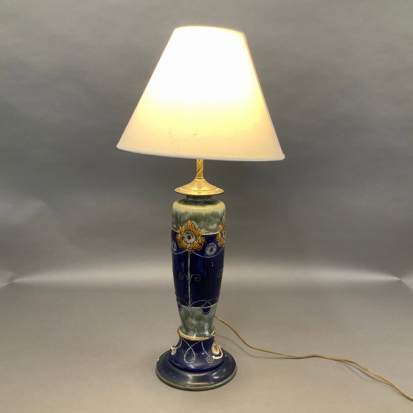 Royal Doulton Lambeth Stoneware Table Lamp with Wooden Base: This Royal Doulton stoneware vase lamp is finished with a deep cobalt blue glaze on the lower section and a mottled sage green glaze on the upper shoulder. The central decoration features raised sunfl