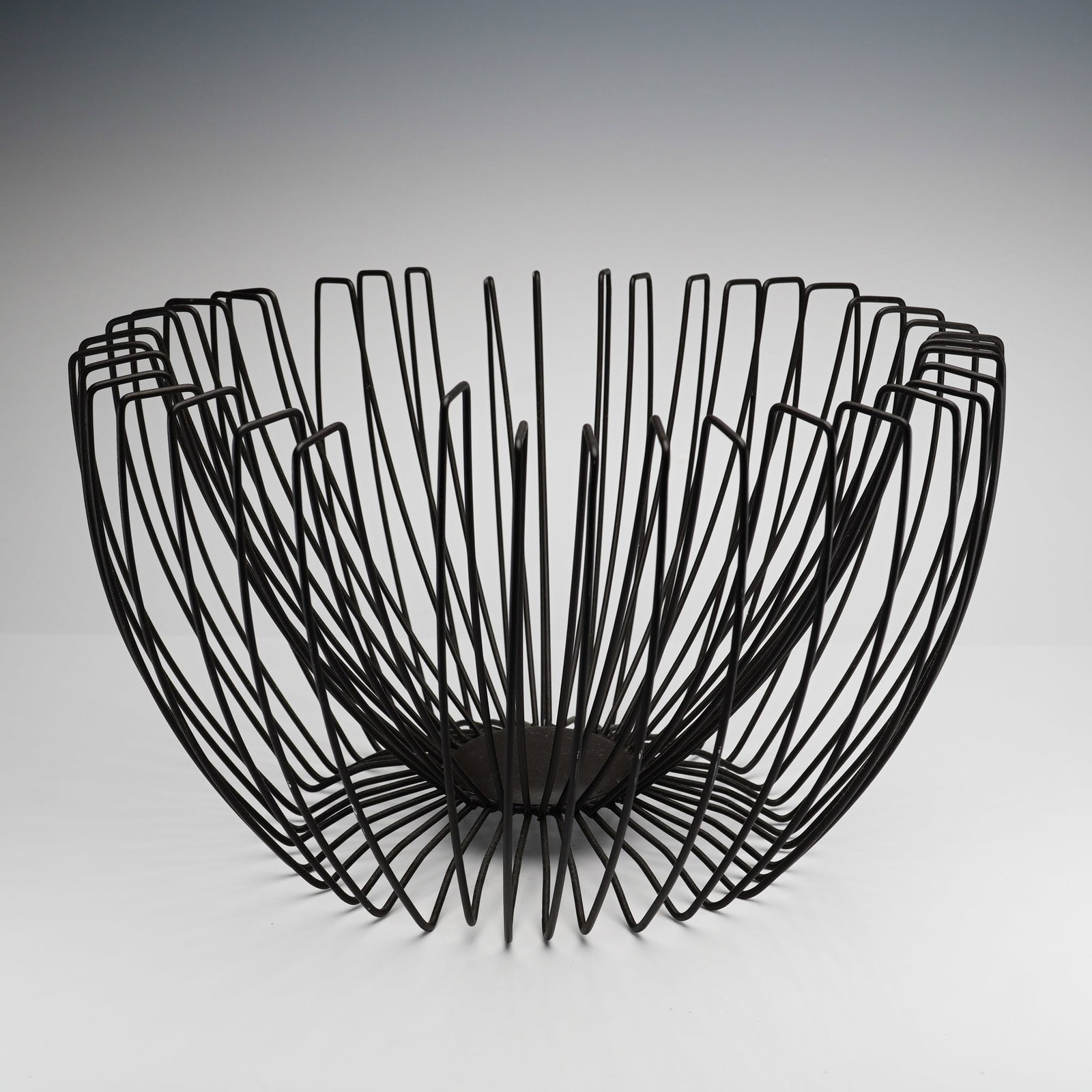 Mid-Century Modern Style Black Finished Metal Wire Fruit Basket: A mid-century style wire basket designed as a modern architectural centerpiece or fruit bowl. This piece features a minimalist, open-wire construction consisting of numerous U-shaped metal ribs of sta