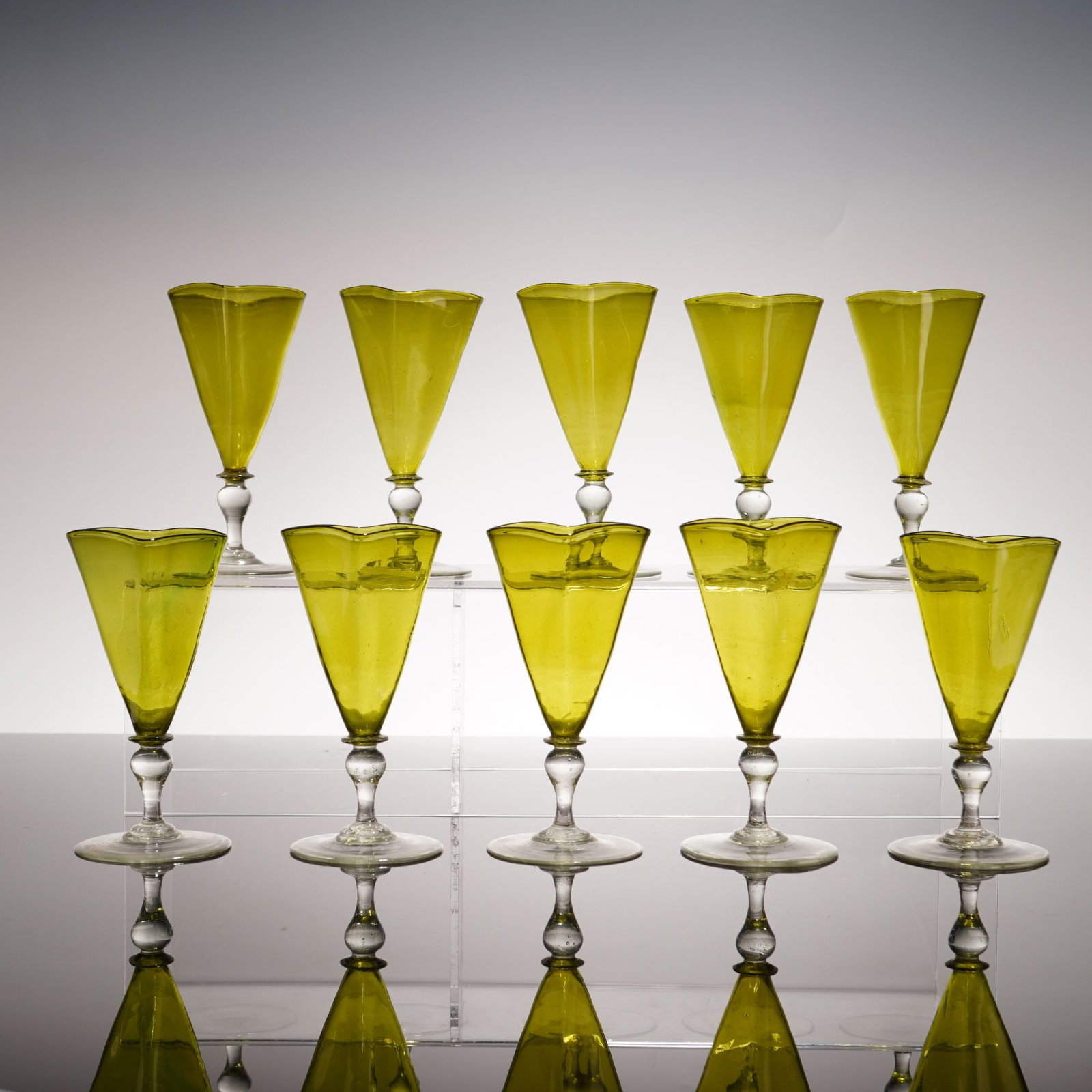 10pc Hand-Blown Glass Cordial Stems with Trefoil Rims: A set of ten hand-blown glass stems, specifically designed for cordial or sherry. Each piece features a translucent olive green glass bowl with a hand-manipulated trefoil rim. The bowls are conical in