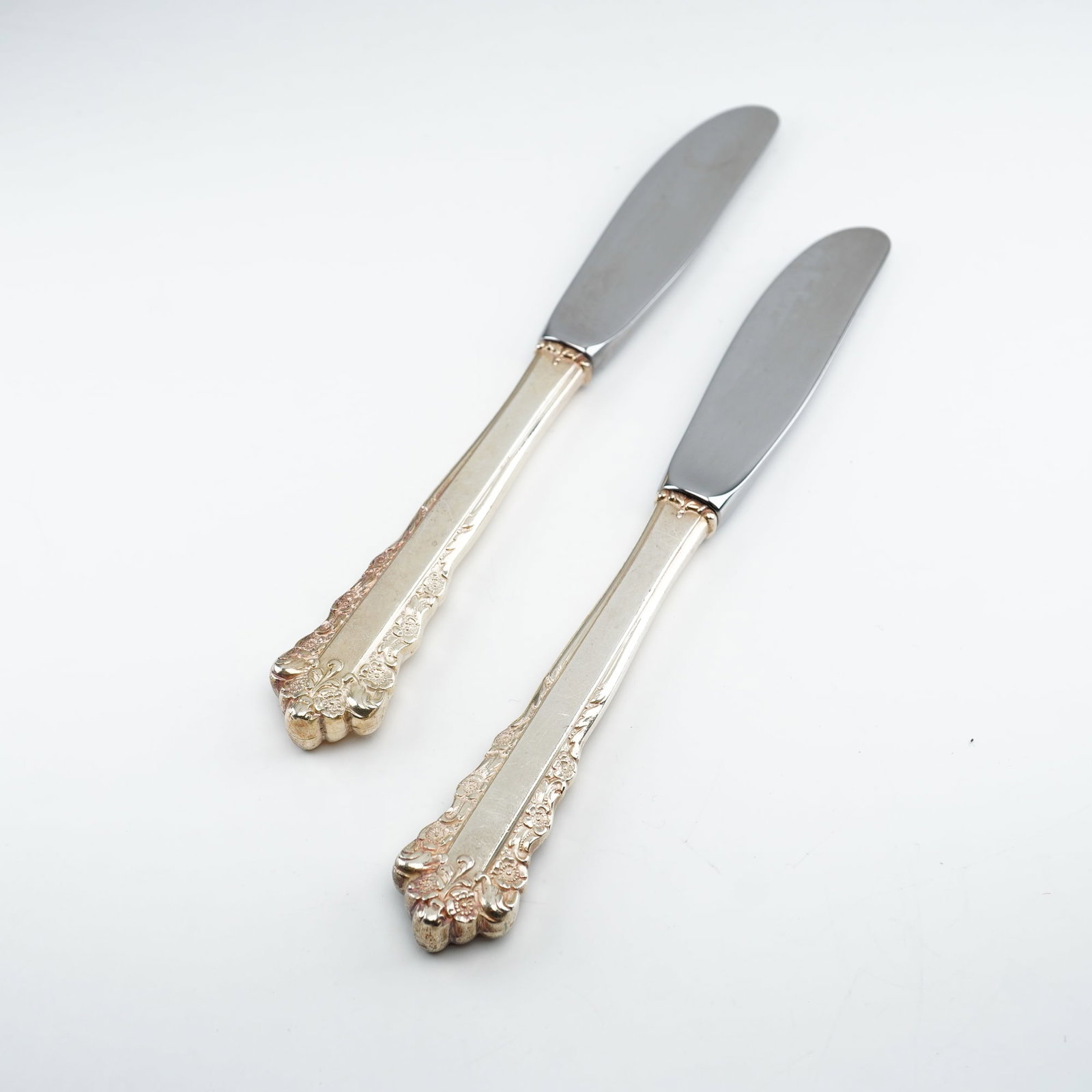 2pc Lunt Sterling Silver and Stainless Steel Butter Spreaders, Belle Meade: Crafted by Lunt Silversmiths between 1967 and 1997, these spreaders showcase an ornate Rococo-style design featuring raised floral clusters and scrolling detail along the handle edges and terminals. T