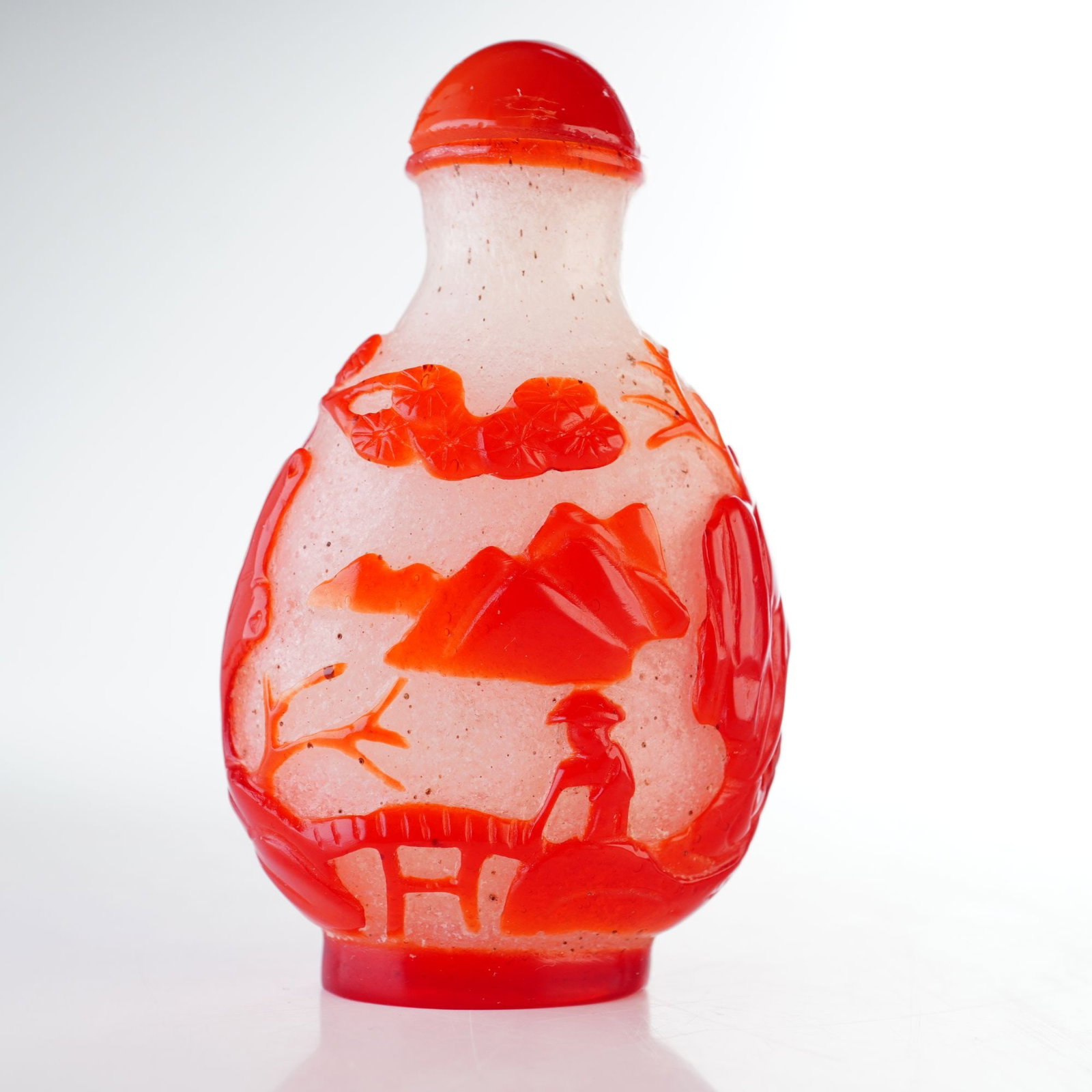 Peking Glass Overlay Snuff Bottle, Red Overlay Landscape with Figures: A clear Peking glass snuff bottle featuring a white and black snowflake pattern, decorated with high-relief red overlay depicting a landscape with figures. It is topped with a domed red stopper. Dimen