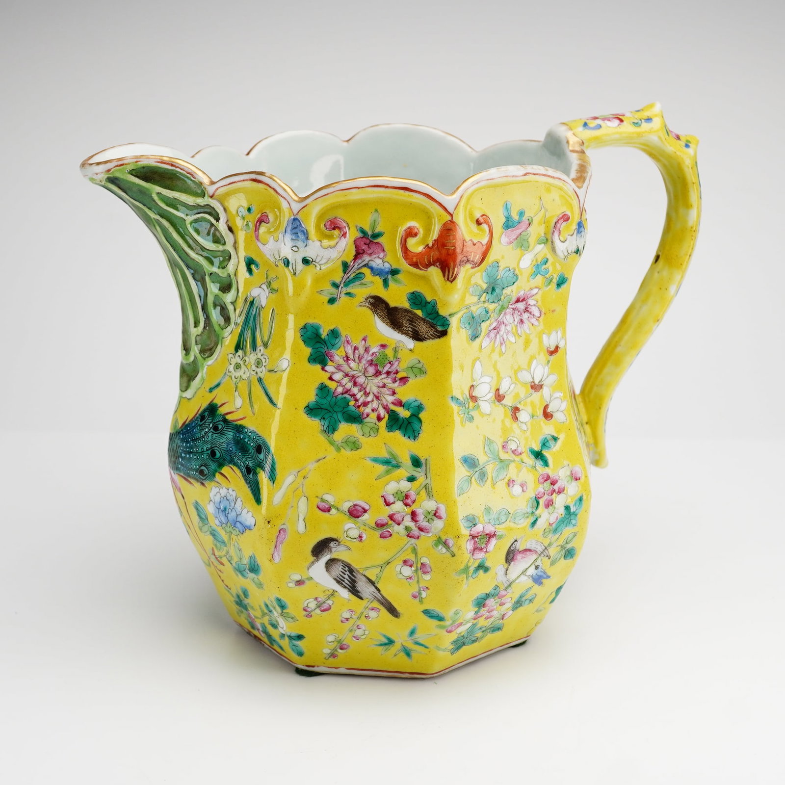 Large Chinese Famille Rose Porcelain Pitcher: A large Chinese porcelain pitcher featuring an octagonal faceted body and a wide scalloped rim. The vessel is designed with a molded cabbage leaf mask spout in shades of green and a twig form handle w