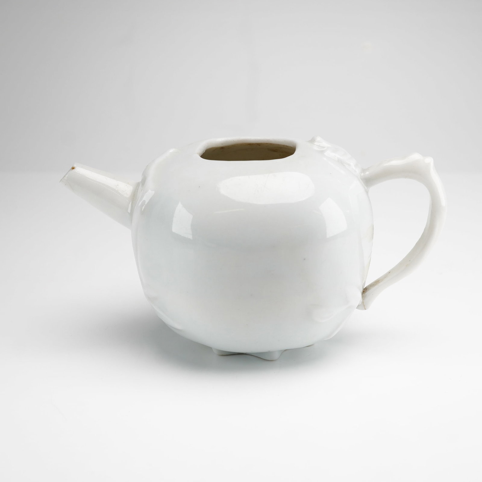 Small Pomegranate-Shaped Porcelain Teapot: A small white glazed porcelain teapot designed in the form of a pomegranate fruit. The globular body is ornamented with applied sprigged floral and foliate motifs. The vessel features a short tapered 