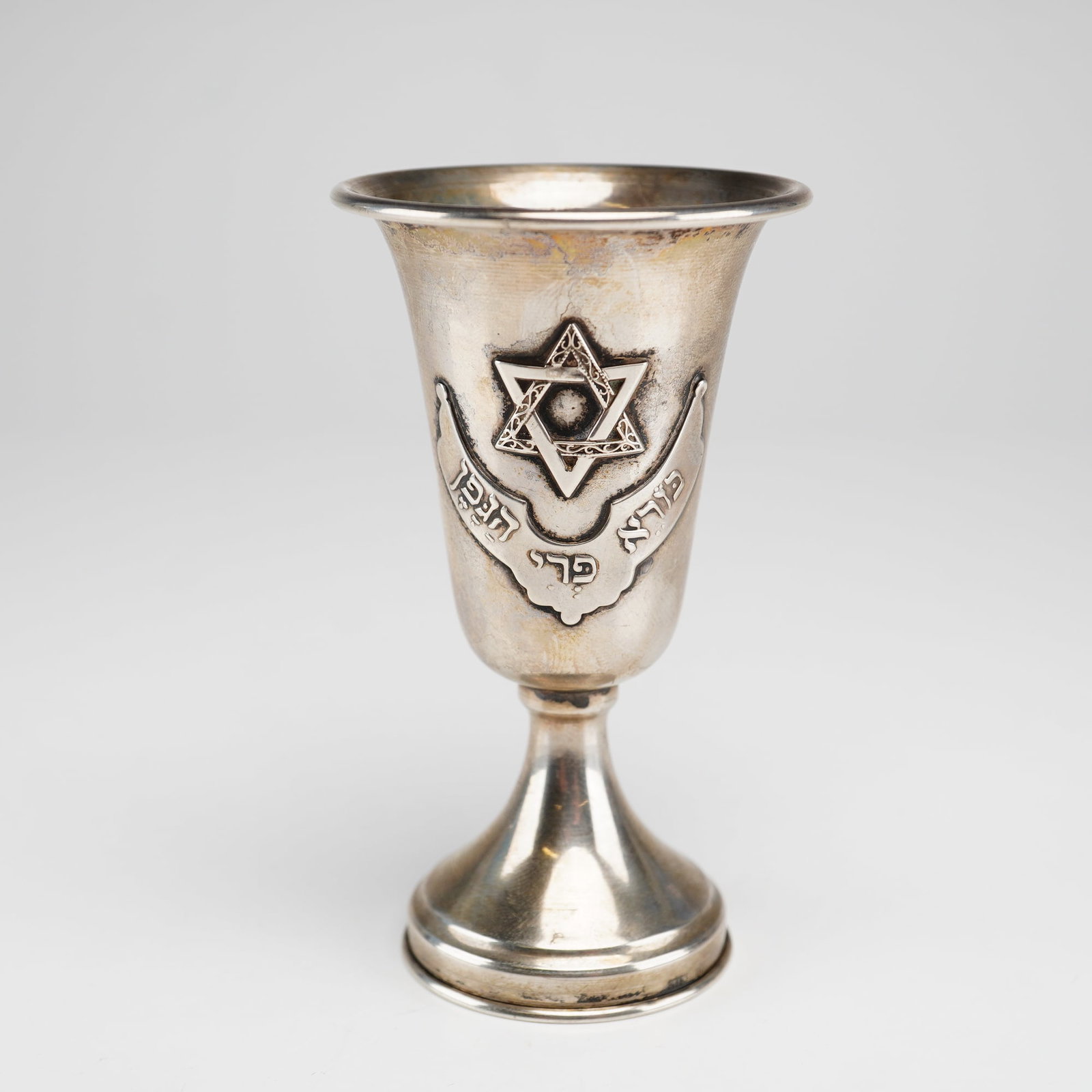 Sterling Silver Kiddush Cup with Applied Filigree Magen David: This sterling silver Kiddush cup features a tapered bowl with a flared rim, set upon a short stem and a stepped circular foot. The front of the bowl is ornamented with an applied Magen David (Star of