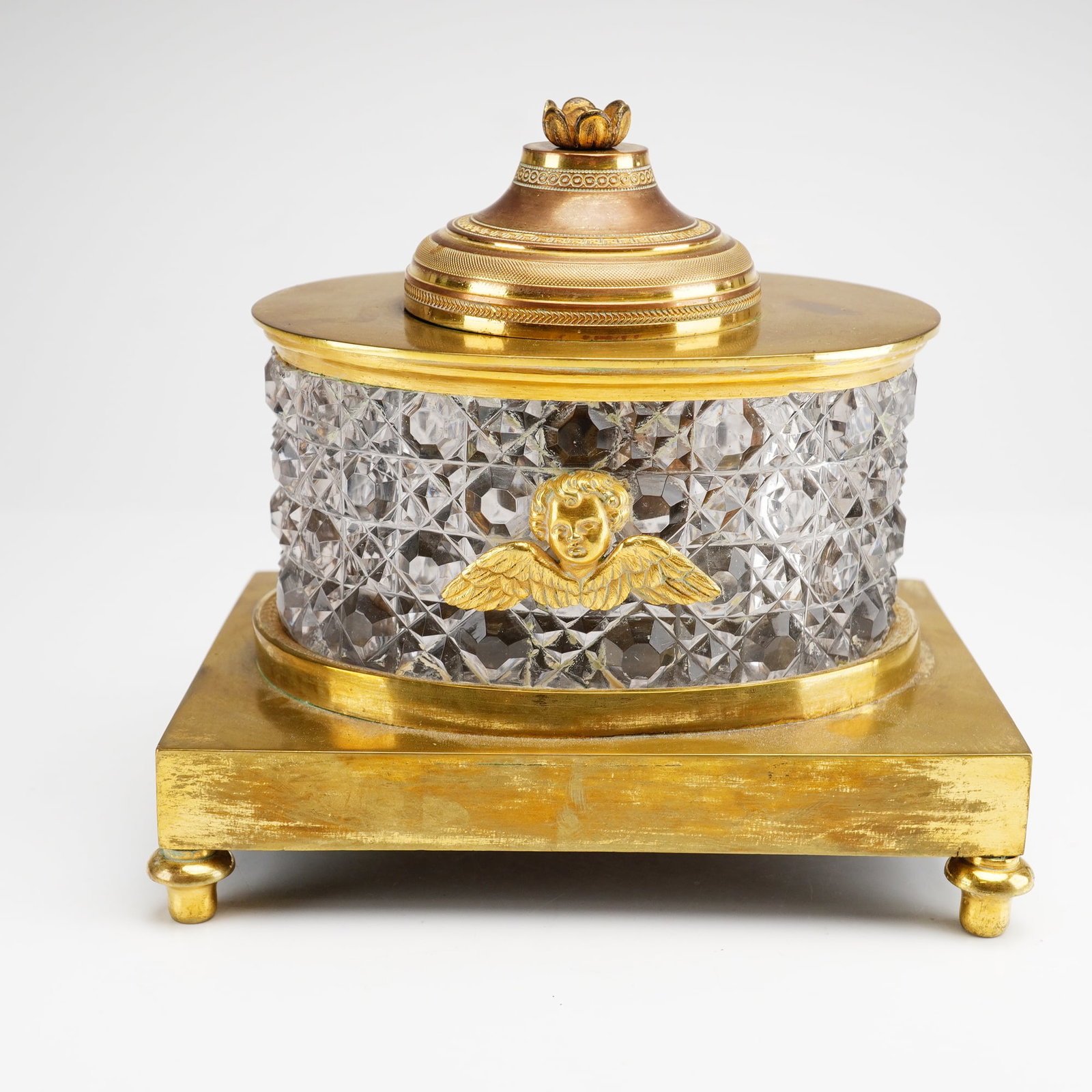 Neoclassical Gilded Brass and Diamond-Cut Crystal Oil Well: This oil well features an oval-shaped heavy crystal body expertly worked in a deep diamond-cut pattern. The front of the vessel is decorated with a cast ormolu mount in the form of a winged cherub