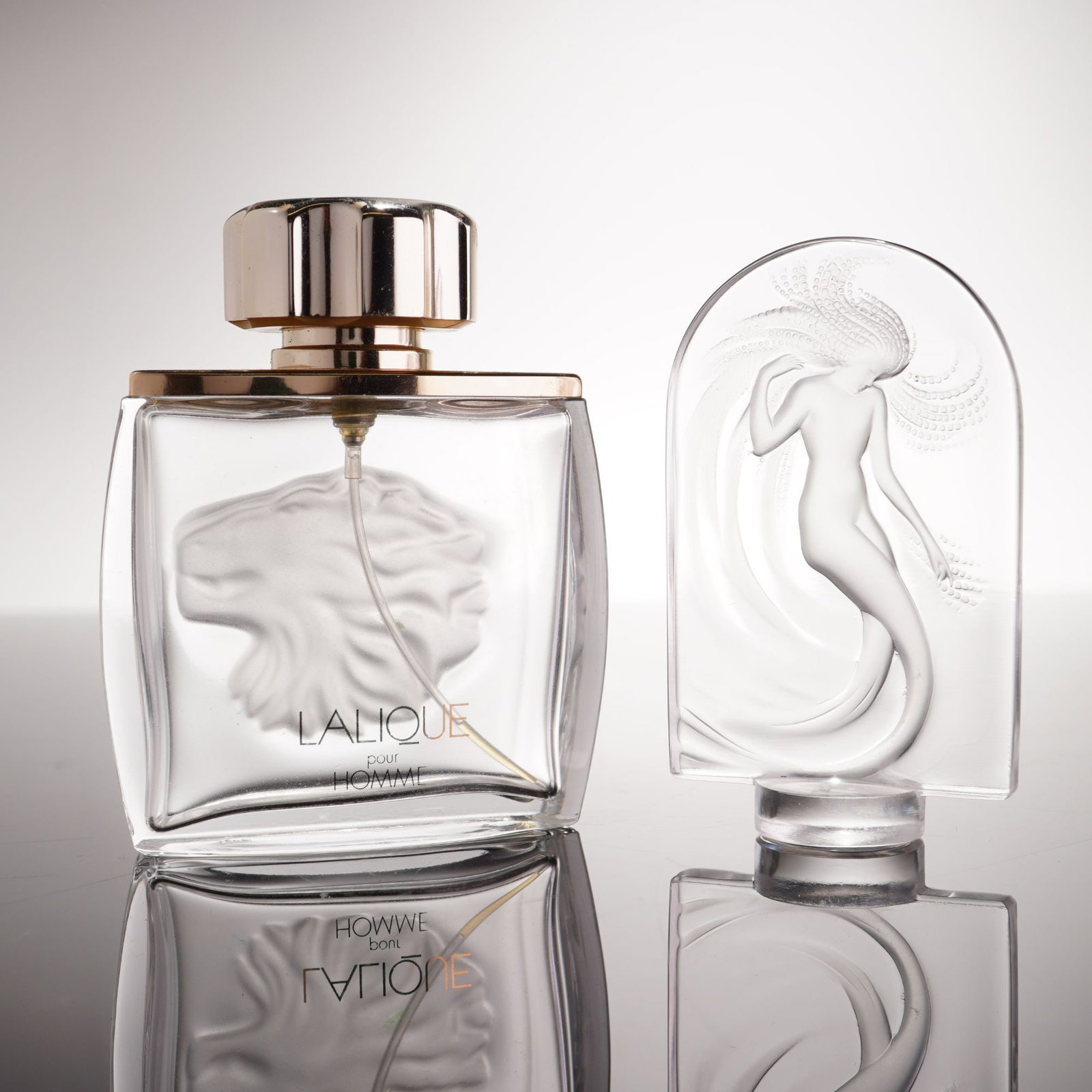 2pc Lalique Crystal Pour Homme Perfume Bottle and Naiade Paperweight: This lot features a 2pc Lalique crystal grouping comprised of a perfume bottle and a decorative paperweight. The first item is a Lalique pour Homme Lion perfume bottle, designed as a rectangular clear