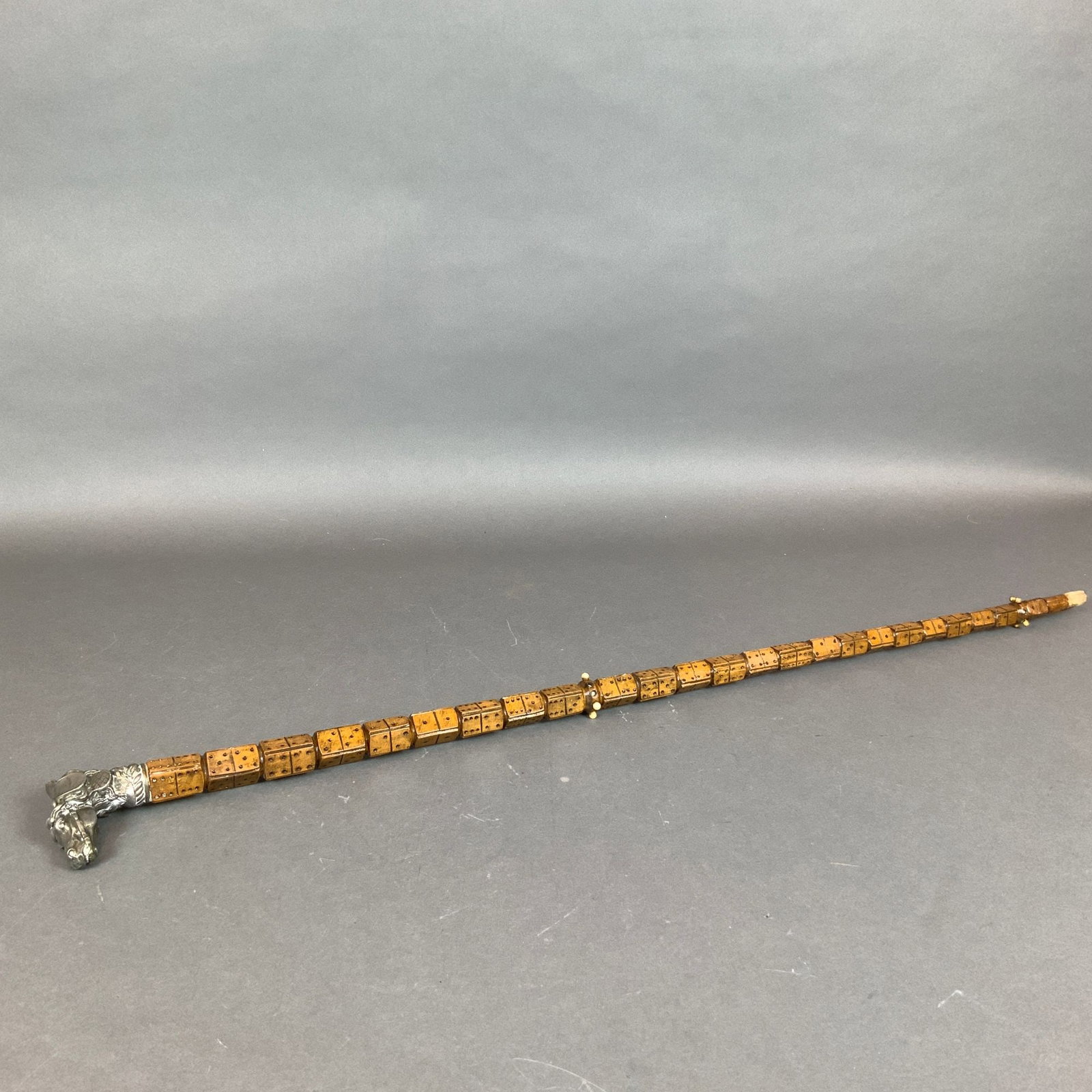 Carved Wood Cane with Dominoes and Metal Horse and Dog Head Handle: This novelty walking cane features a shaft constructed from stacked, rectangular segments of carved wood decorated with pips in a domino pattern. The handle is cast in a silver-toned metal