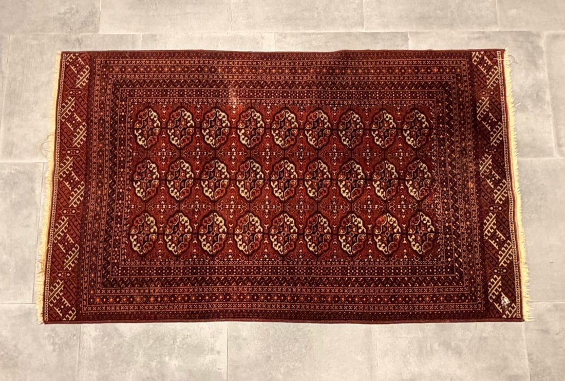 Antique Persian Turkoman Style Bukhara Hand-Knotted Wool Rug: This hand-knotted antique Persian Turkoman style rug features a traditional Bukhara design. Constructed with a wool pile on a cotton foundation, the rug centers a vibrant madder-red field decorated