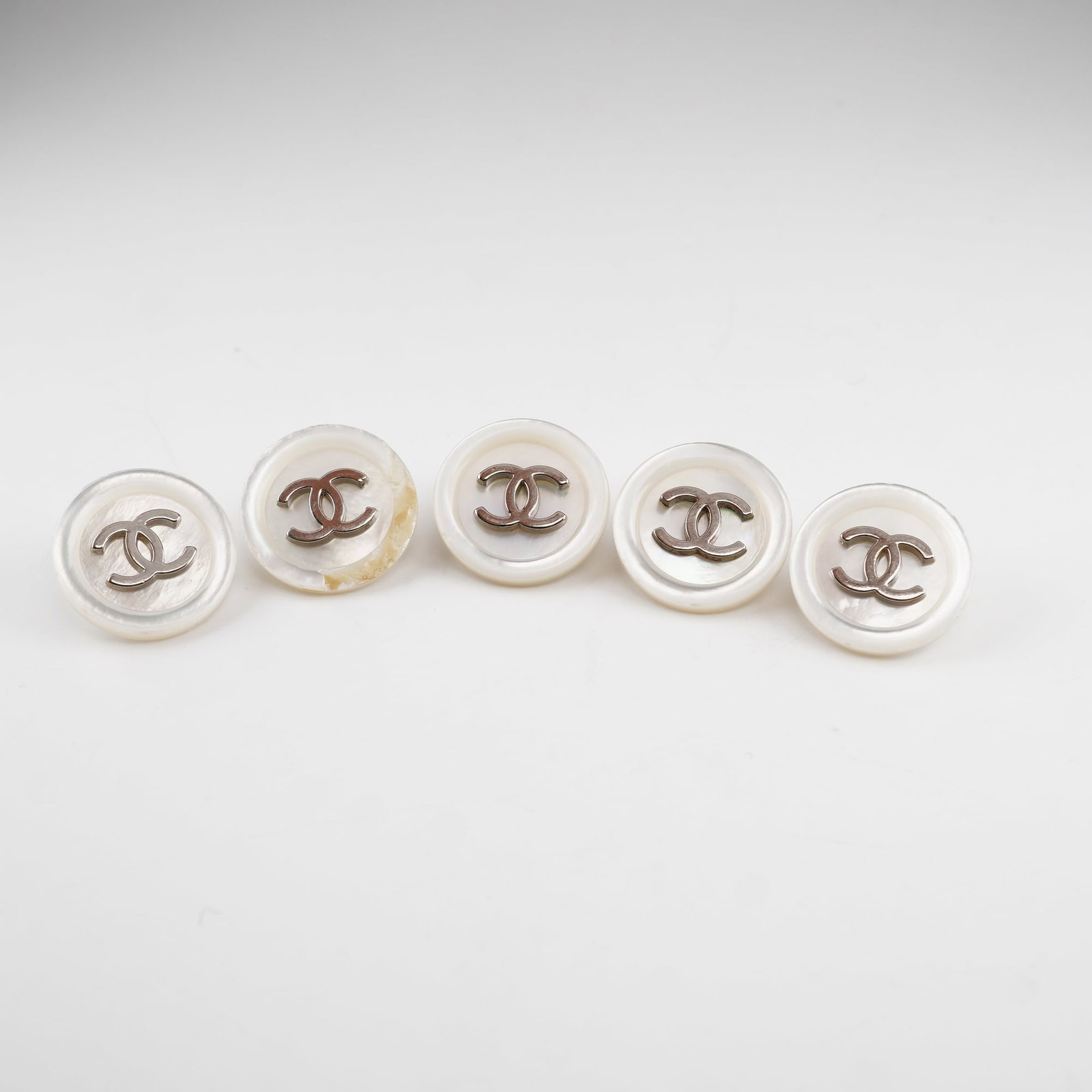 5pc Chanel Opalescent Round Buttons: A set of 5 Chanel designer buttons in a round pearlescent colors with the Chanel logo in a silver-tone. The reverse side is also in a silver-tone with the impressed stamp Chanel. Dimensions: Each butt