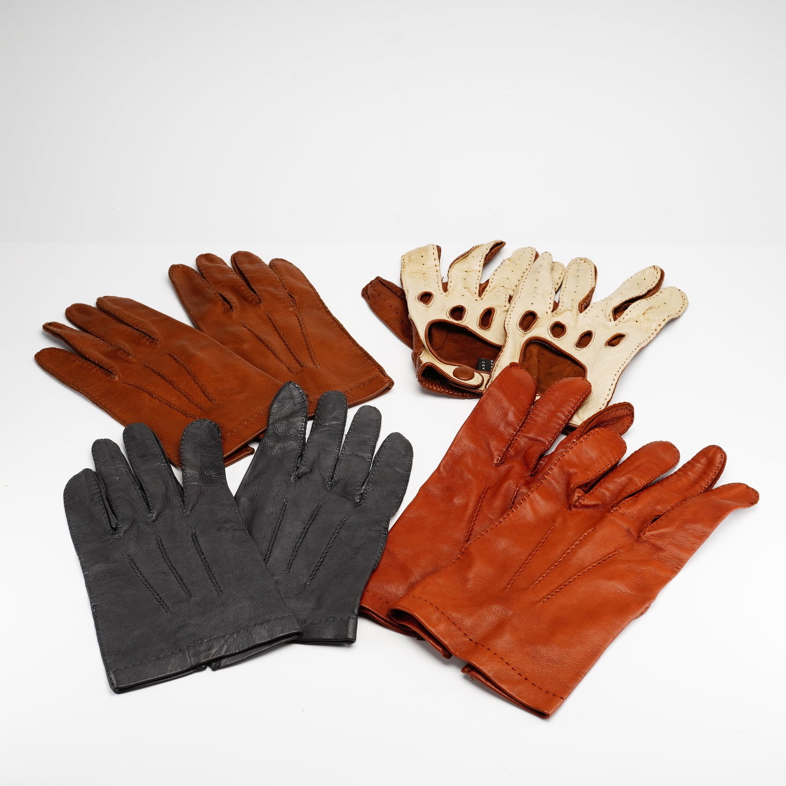 Four Pairs of Ladies Leather Gloves: A collection of four pairs of ladies leather gloves in a medium size. The assortment includes a pair of smooth dark grey dress gloves with three rows of decorative topstitching on the back, a pair of 