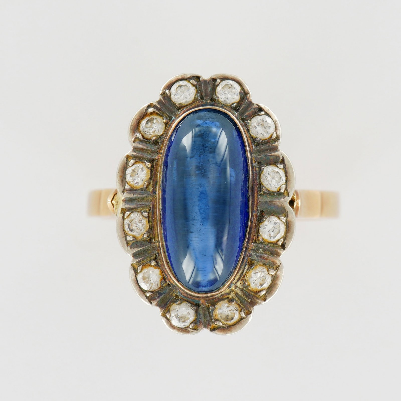 14K Gold Ring with Cabochon Lab Sapphire and Diamond Halo: An elegant 14k yellow gold ring showcasing a luminous 2.5-carat oval cabochon lab sapphire of deep cornflower blue hue. The center stone is framed by a scalloped halo of old-cut diamonds totaling appr