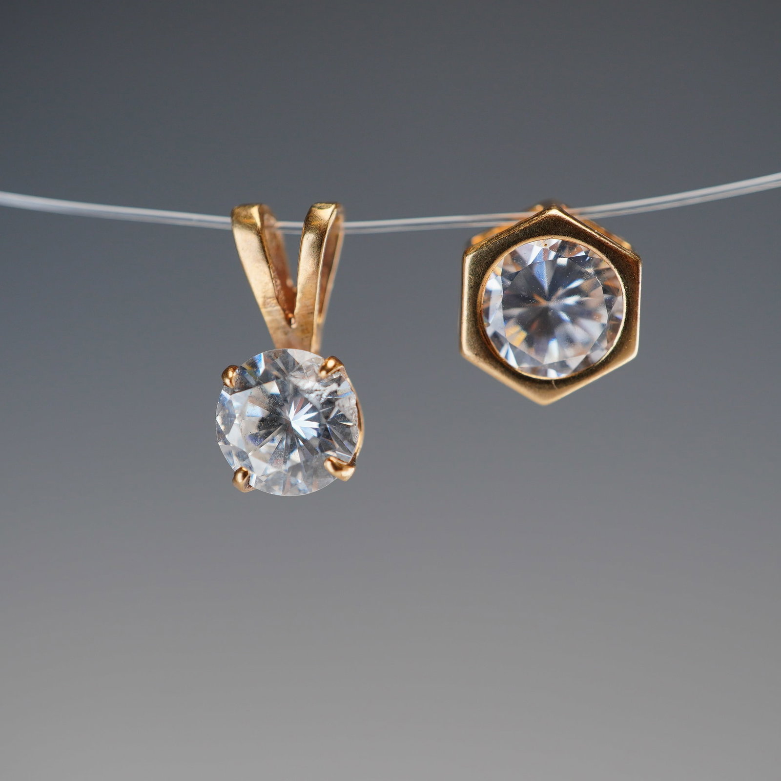 2pc 14K Gold Round Clear Stone Solitaire Pendants: This lot features a group of pendants crafted from 14K yellow gold. One pendant showcases a round brilliant-cut clear stone in a four-prong setting with a V-shaped bail. The second is a hexagonal-shap