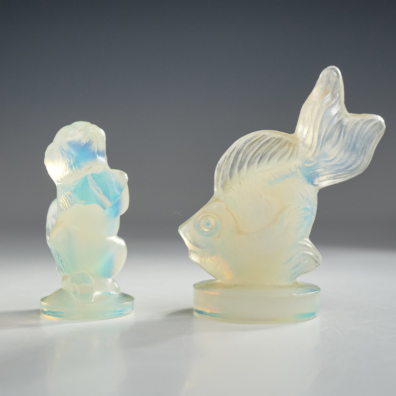 2pc Sabino Opalescent Art Glass Figurines, Veiltail Fish and Pekingese Dog: This lot features two miniature opalescent art glass figurines produced by Sabino in France. The set includes a veiltail fish captured in a dynamic mid-swim pose with large, flowing fins, and a Peking