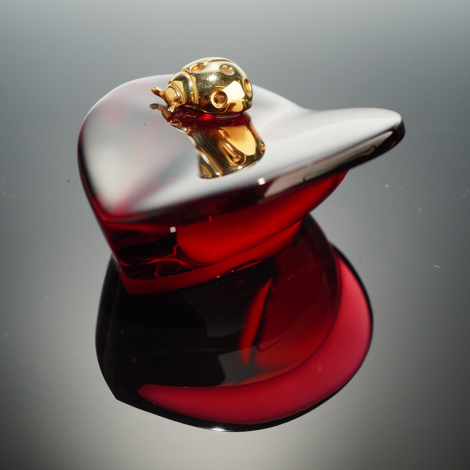 Baccarat Ruby Red Crystal Heart Paperweight with Gilded Ladybug: A ruby red crystal paperweight by Baccarat, designed in the form of a heart. The piece features a gilded metal ladybug figurine mounted to the top surface, detailed with recessed spots. The deep red c