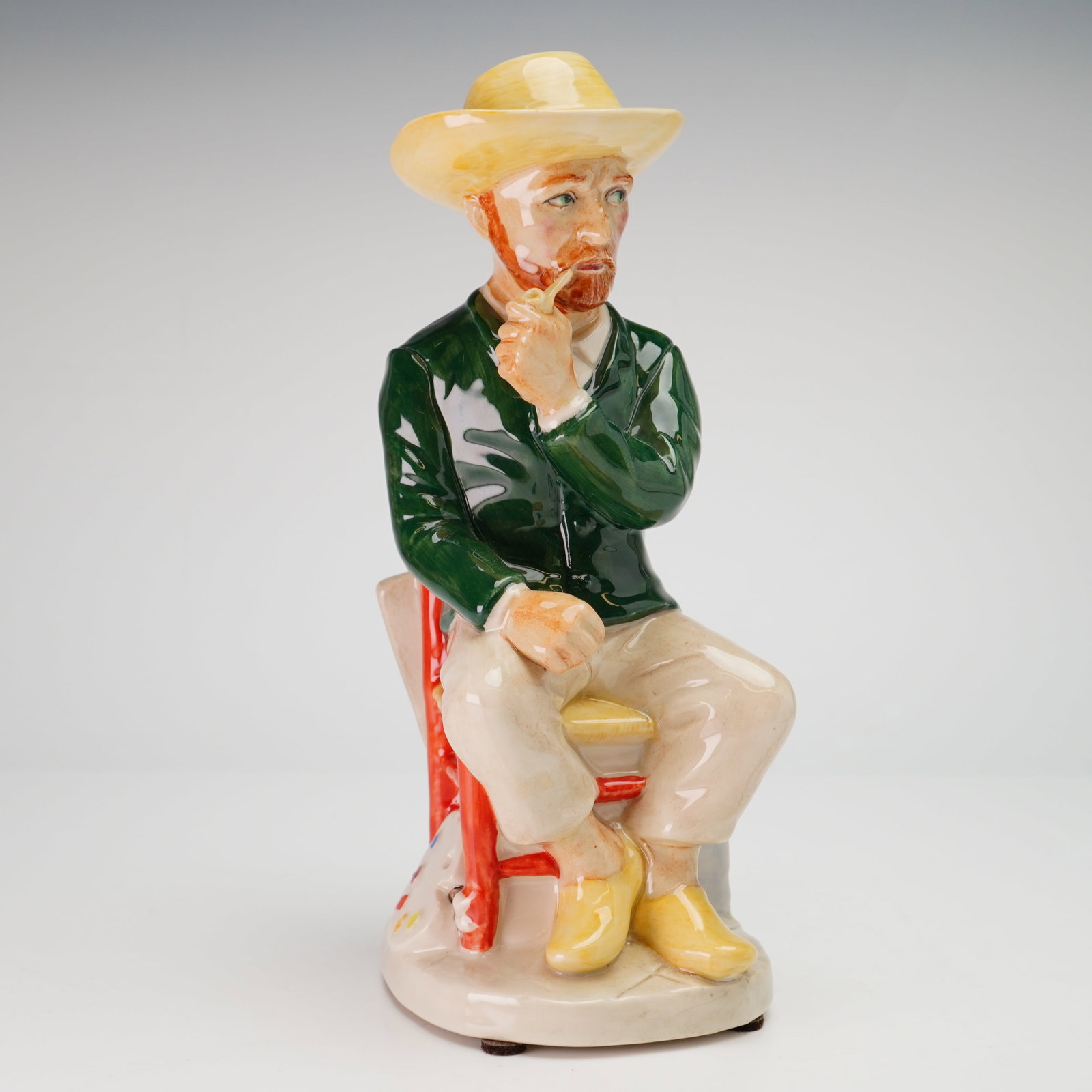 Kevin Francis Ceramics Limited Edition Toby Jug, Vincent van Gogh: The figurine depicts the artist Vincent van Gogh seated on a red rustic chair while smoking a pipe. He is modeled wearing a yellow straw hat, a dark green jacket, light tan trousers, and yellow clogs.