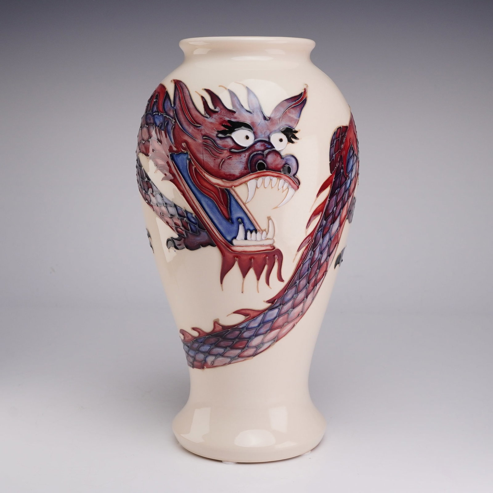 Moorcroft Pottery by Trevor Critchlow Vase, Dragon Pattern: This Moorcroft ceramic vase features the Dragon pattern, designed by Trevor Critchlow. The baluster-form vase is finished in a cream-colored ground and decorated with a wrap-around dragon motif. The d