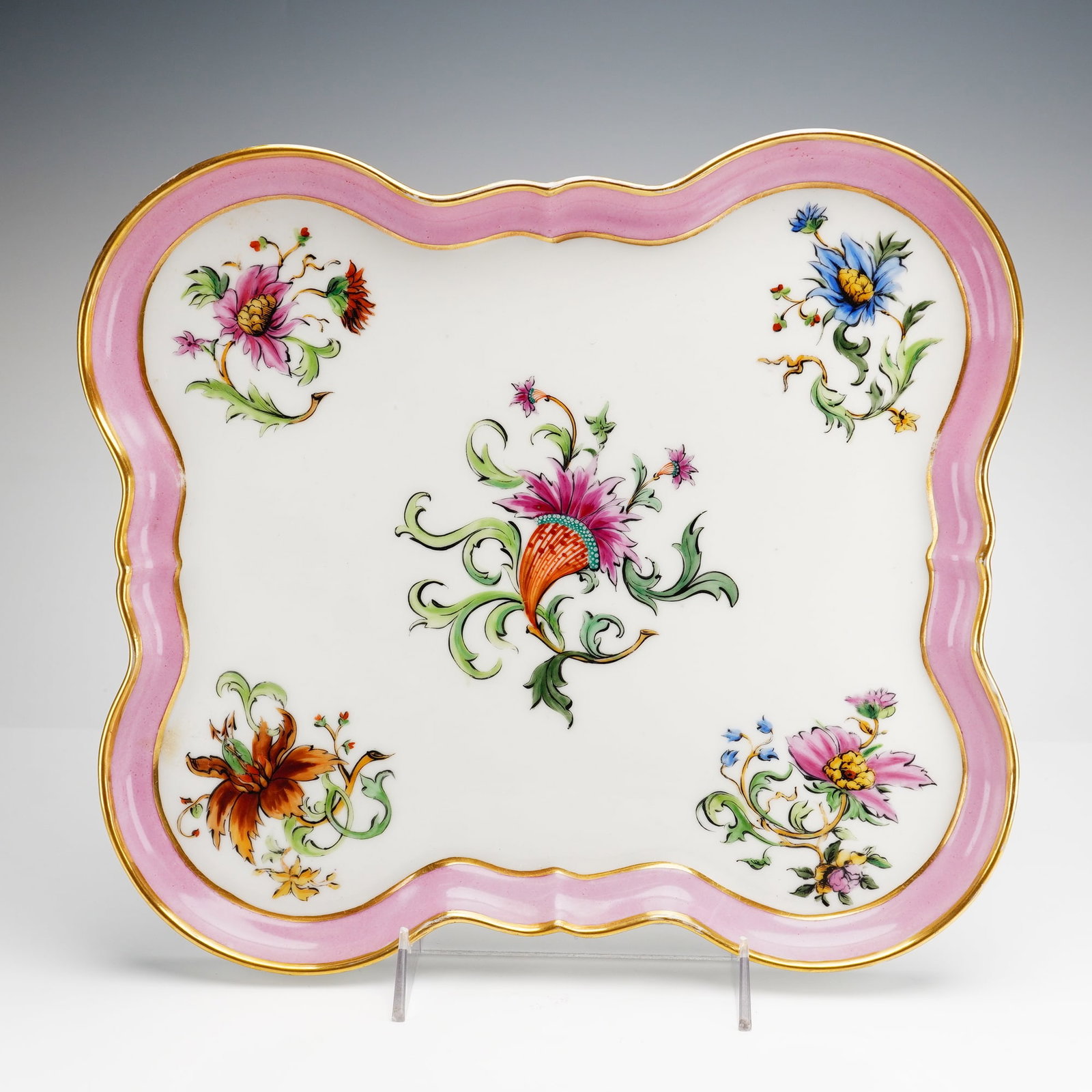 Large Hand-Painted Porcelain Serving Tray: This large hand-painted porcelain tray features a shallow square form with a scalloped and lobed rim, creating an undulating profile. The tray is decorated in the Rococo style with a wide rose-pink bo