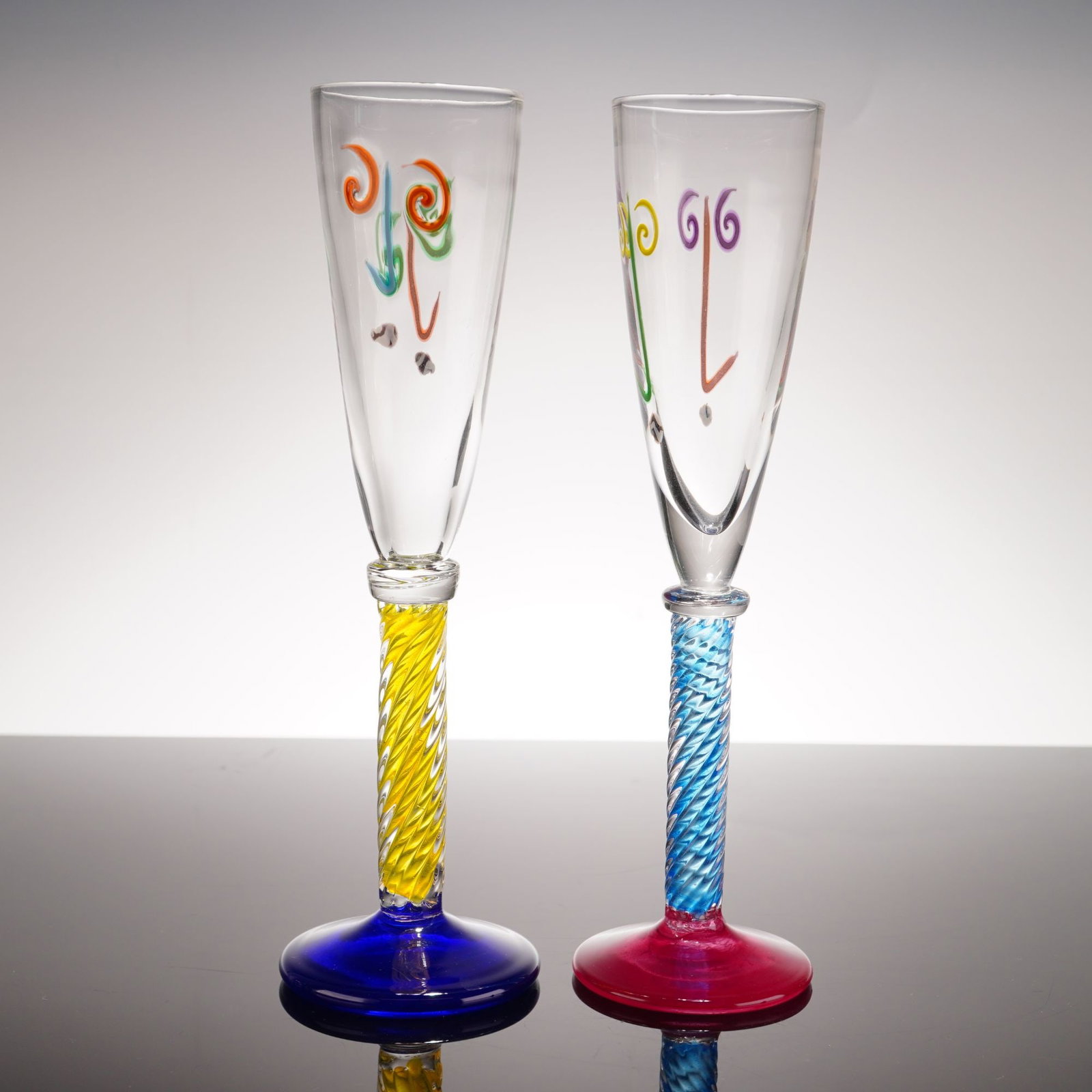 Pair of Art Glass Champagne Flutes by Fun Time Studios, 1992: This pair of hand-made multi-colored art glass champagne flutes were create in 1992 by Fun Time Studios. Each piece features a hand-blown clear glass bowl decorated with hand-applied glass trails and 