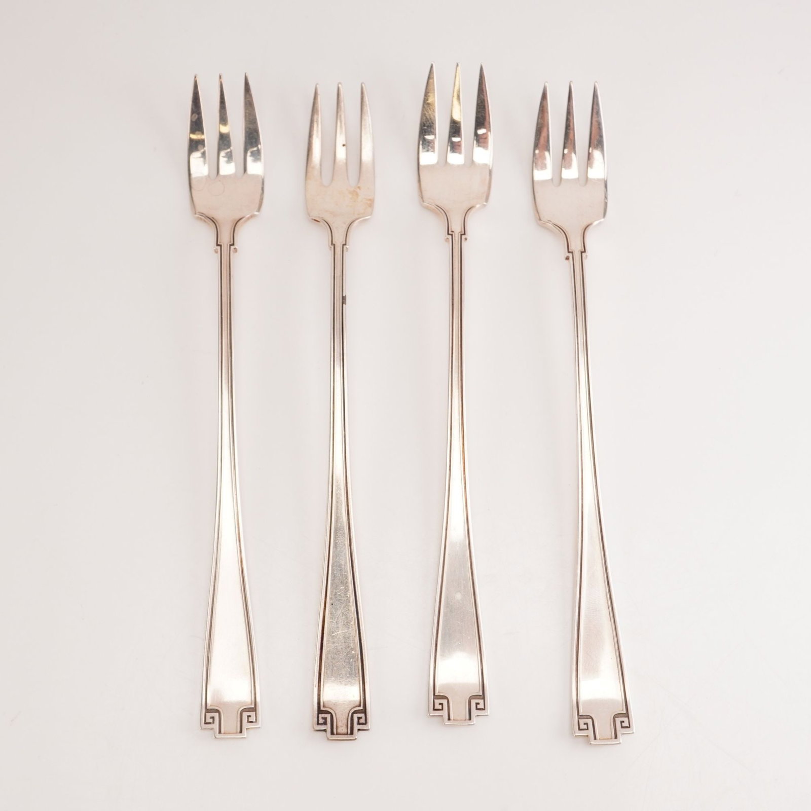 4pc Gorham Sterling Silver Cocktail Forks, Etruscan: This 4-piece set of Gorham sterling silver cocktail forks is presented in the Etruscan pattern, produced from 1913 to 1991. Inspired by Greco-Roman revival styling, the pattern features a balanced geo