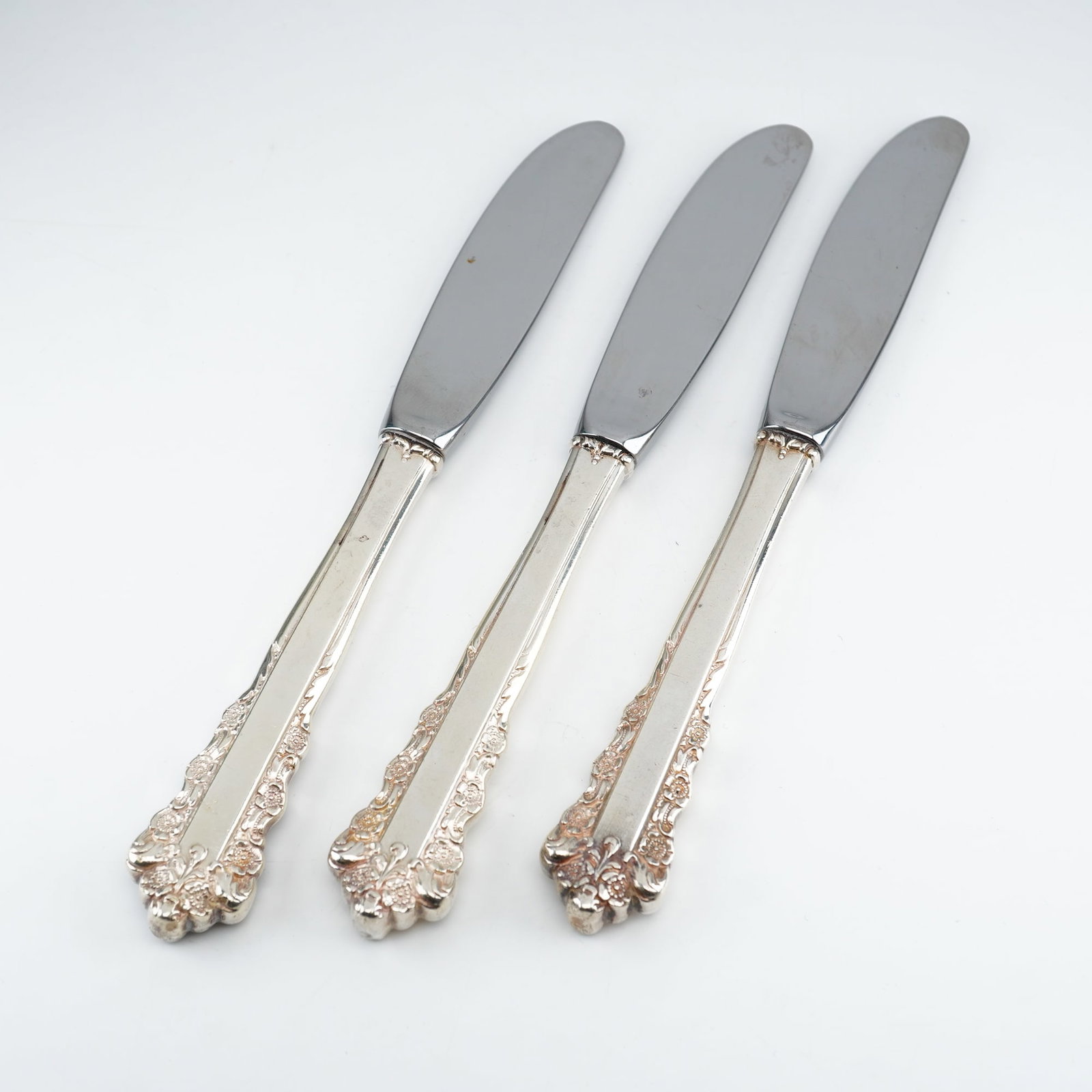 2pc Lunt Sterling Silver and Stainless Steel Butter Spreaders, Belle Meade: Crafted by Lunt Silversmiths from 1967"1997, each piece features an ornate Rococo-inspired design with raised floral clusters and elegant scrolling along the handle edges and terminals. The handles ar