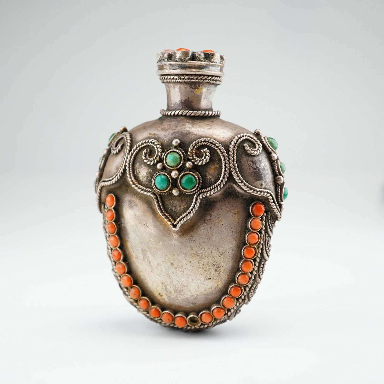 Mongolian Silver Repousse Snuff Bottle, Ruyi Head Design, Rounded Bottom: Decorated with coral and turquoise stones, this Mongolian silver repousse snuff bottle with stopper features a Ruyi head pattern along the top, a braided rope design along the sides and curved bottom,