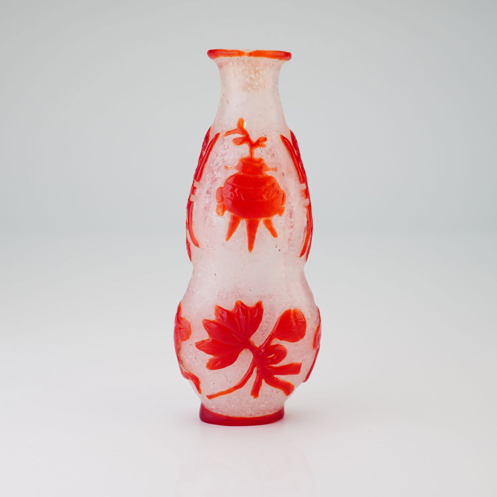 Peking Glass Snuff Bottle, Red Overlay Auspicious Symbols, Double Gourd Form: Featuring a red relief overlay, this clear snowflake Peking glass snuff bottle takes the shape of a double gourd and depicts auspicious symbols. Dimensions: 1.5"L x 0.75"W x 3.5"H Weight: 1.8 oz