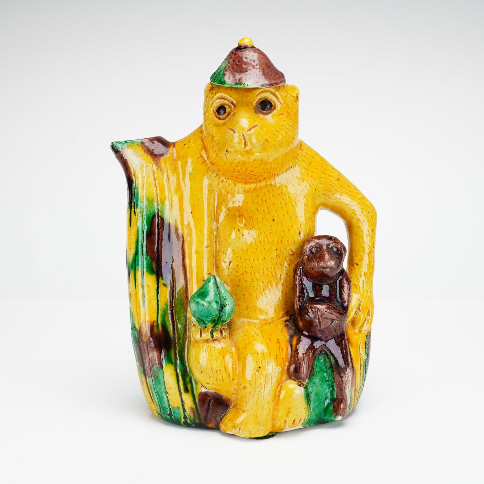 Chinese Sancai Glazed Monkey Teapot: A whimsical glazed ceramic figural pitcher modeled as a yellow monkey seated beside a tree stump, with a smaller brown monkey resting on its lap. The piece is decorated in vibrant yellow, green, and b