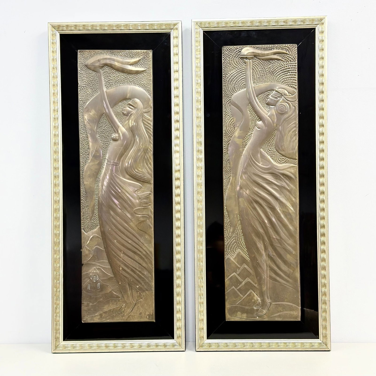 A Pair of Art Deco Style Copper Relief Wall Hangings: A pair of copper relief decorative wall hangings depicting stylized women in the Art Deco style. Each plaque features an elongated female figure in profile with flowing hair and garments, rendered in