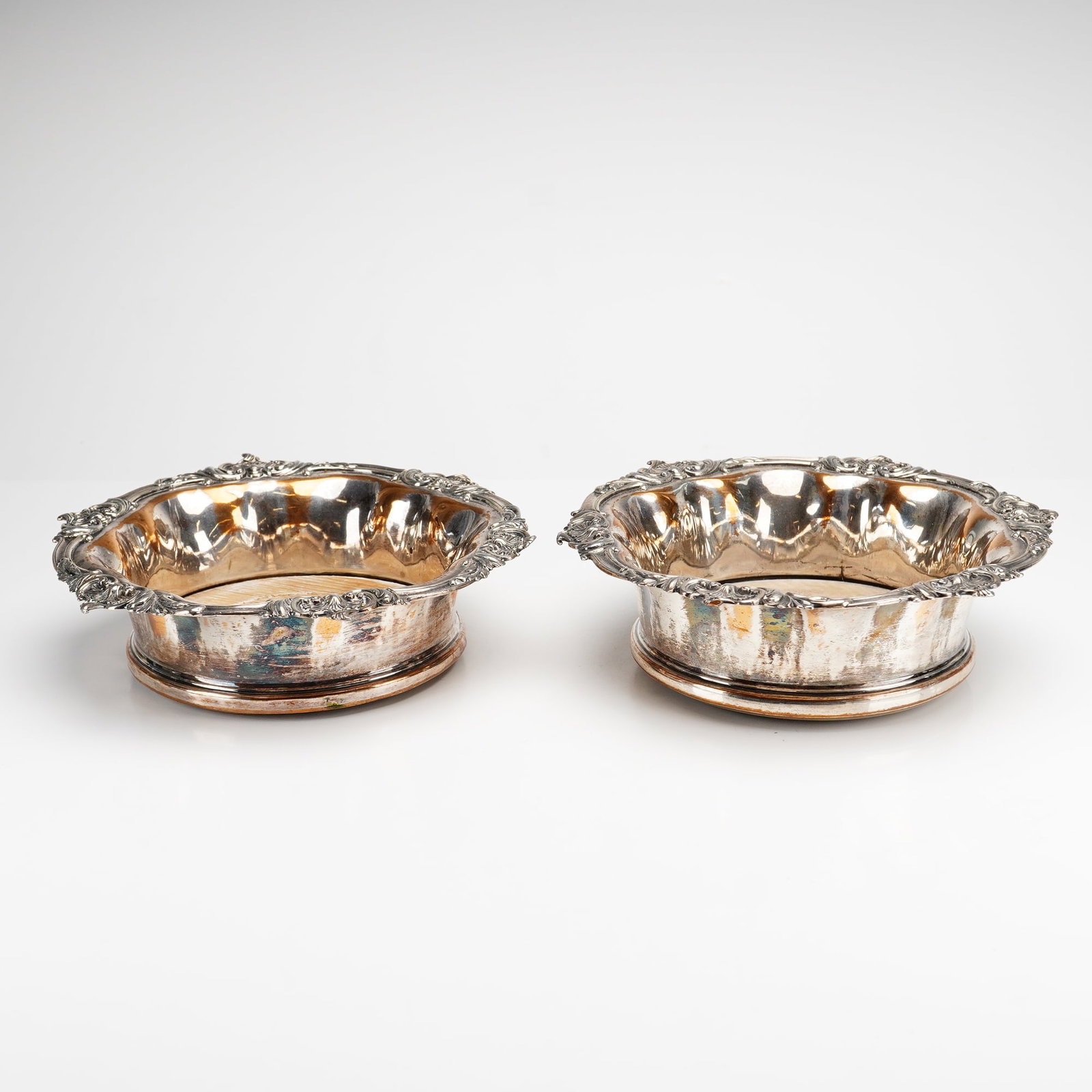 2pc Silver-Plated and Wood Rococo Revival Style Champagne Coasters: This pair of silver-plated champagne coasters features a circular form with turned wood bases. Each coaster is designed with a wide, flared rim adorned with cast and applied Rococo Revival