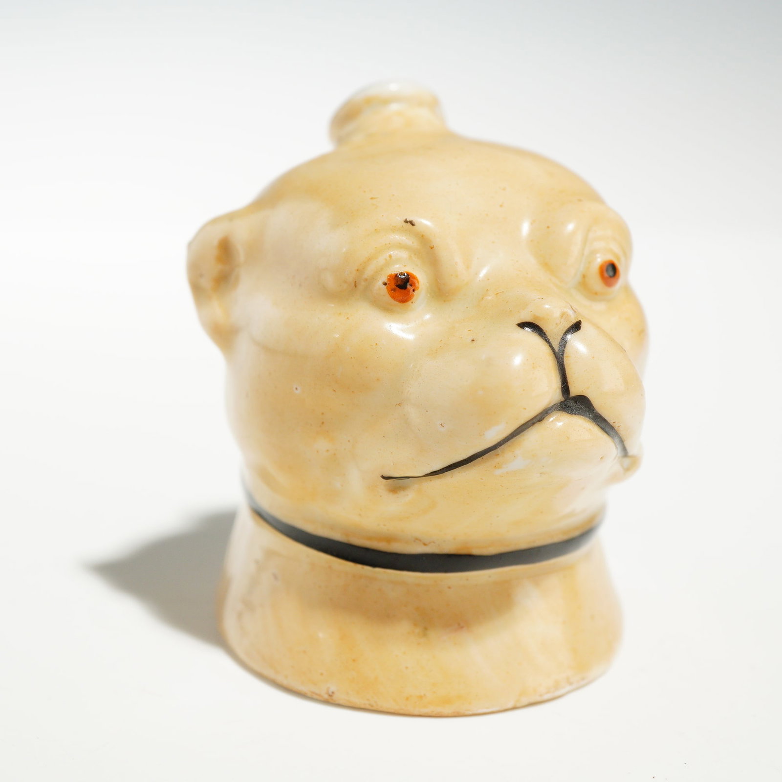 Antique Ceramic Pug's Head Toothpick Holder: A novelty ceramic miniature toothpick holder designed in the form of a pug's head. The piece features a glossy cream-colored glaze with subtle mottled yellowish-brown undertones throughout. The