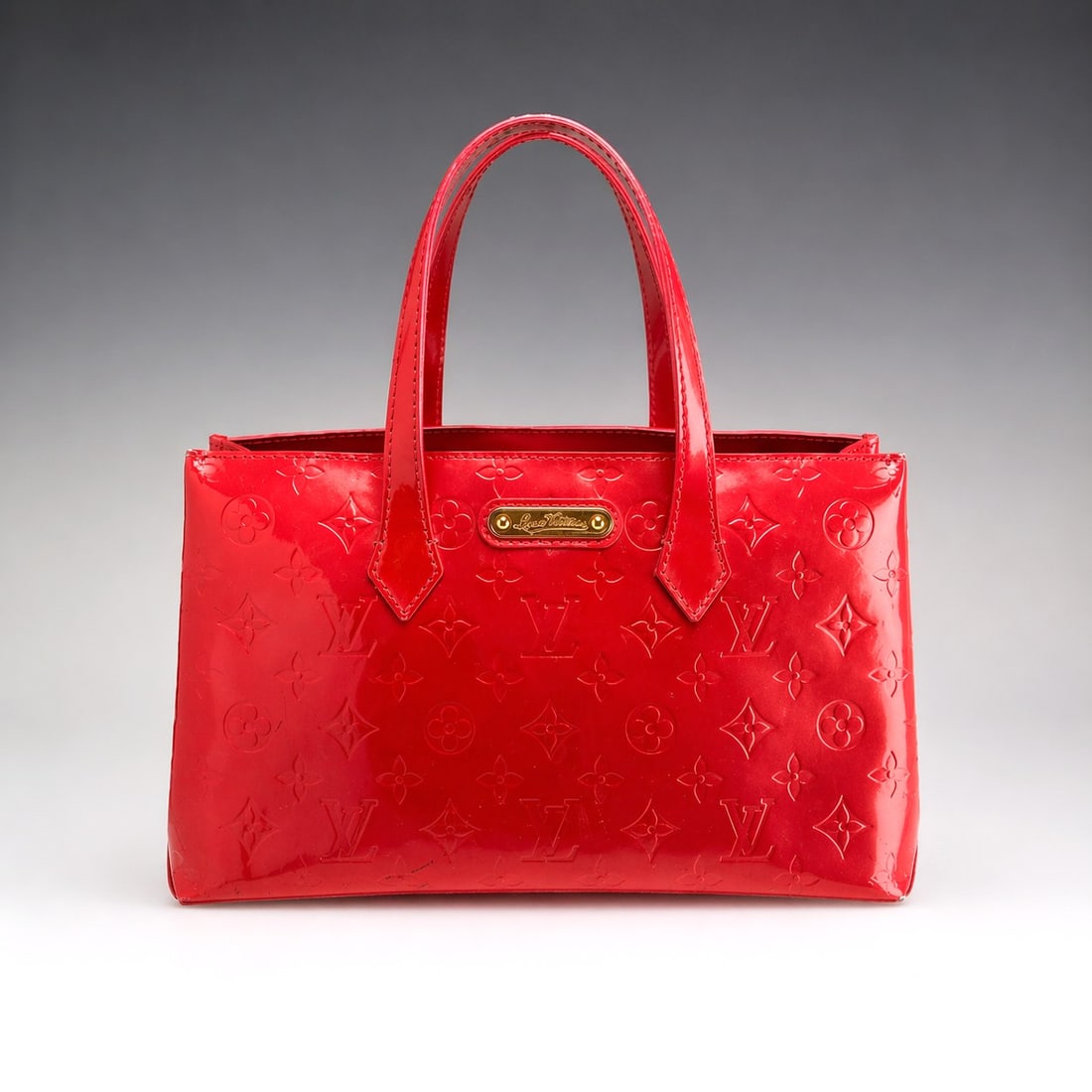 Louis Vuitton Monogram Vernis Wilshire PM Handbag in Red: This Louis Vuitton Wilshire PM handbag is crafted from red Monogram Vernis patent calf leather, featuring the signature LV monogram and floral motifs embossed throughout the exterior. The tote bag des