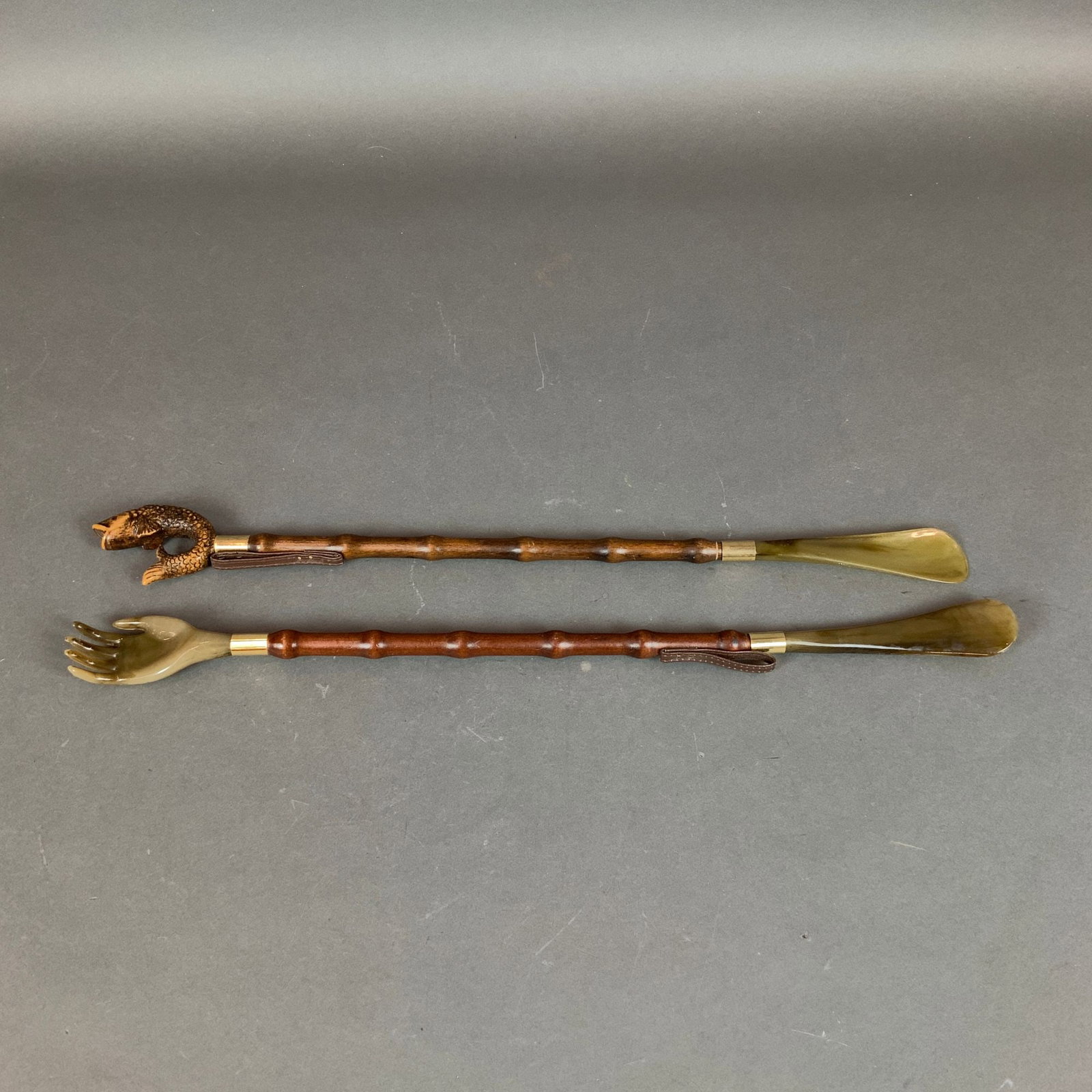 2pc Wooden Shoe Horns with Faux-Bamboo Shafts and Carved Finials: A pair of long-handled shoehorns featuring turned wooden shafts designed in a faux-bamboo style with a dark reddish-brown finish. One implement is a dual-purpose tool, terminating in a carved transluc