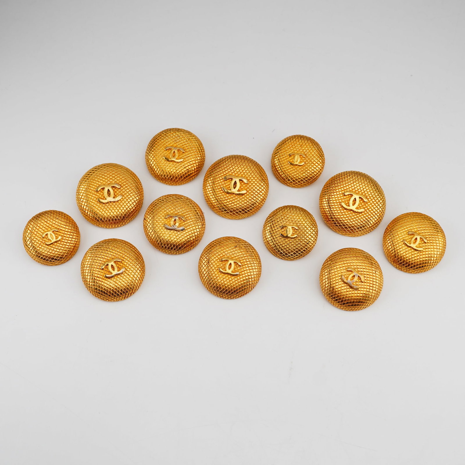 12pc Chanel Golden Metal Round Buttons: A set of 12 Chanel designer metal buttons in gold-tone, featuring a quilted texture and iconic interlocking CC Chanel logo. The reverse side features the impressed stamp Chanel. Dimensions: Each
