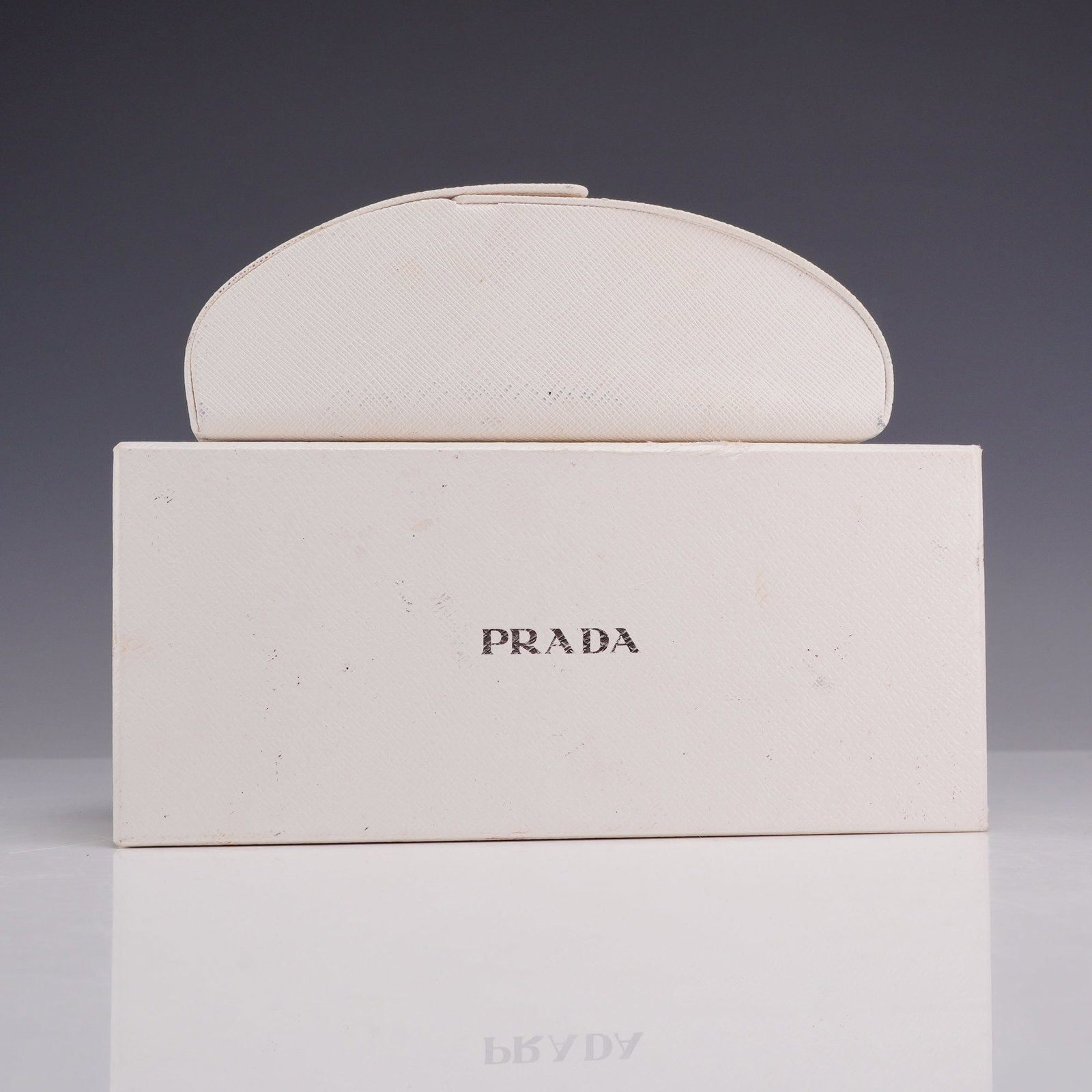 Prada Eyewear Case and Presentation Box: This lot features a Prada eyewear case and its matching presentation box. Both items are finished in a white textured material resembling Saffiano leather. The hard-shell case is designed with a