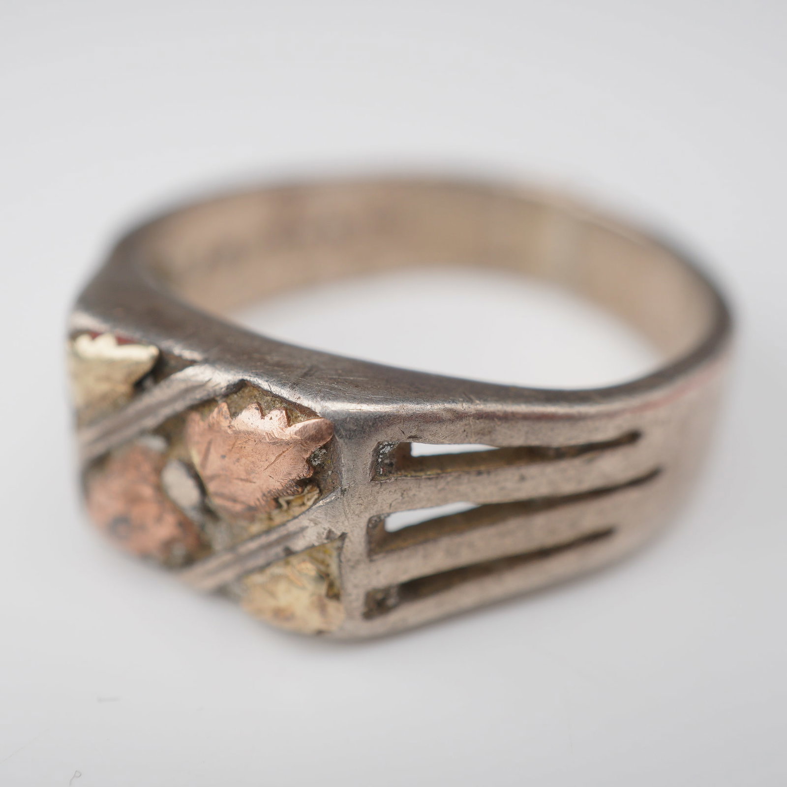 Sterling Silver and 10K Gold Signet Style Ring: This signet style ring features a sterling silver band with decorative 10-karat yellow and rose gold leaf appliques. The central rectangular face is designed with a textured background that holds four