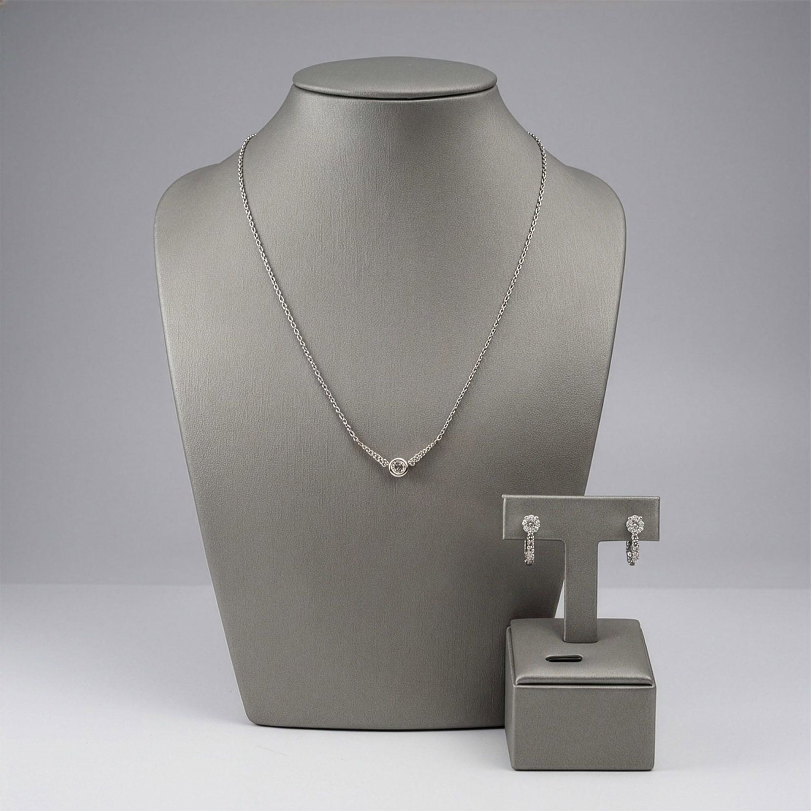 3pc 14K White Gold and Diamond Necklace and Earring Jewelry Suite: A 14K white gold and diamond jewelry suite consisting of a pendant necklace and a pair of matching lever-back earrings. The necklace features an integrated, curved bar pendant with a central round bri