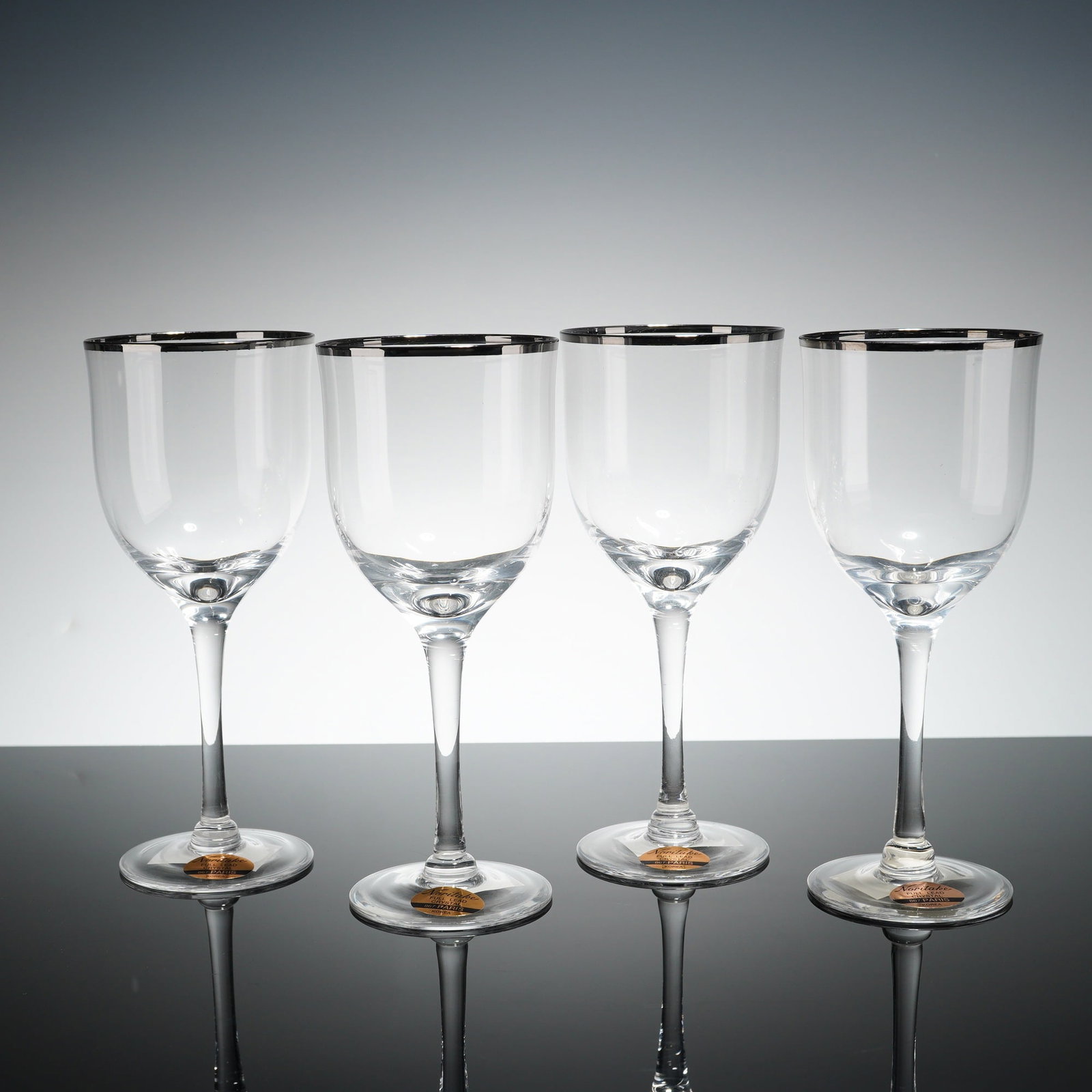 4pc Noritake Platinum Rimmed Crystal Wine Glasses, Paris: Crystal glasses in the Paris pattern, number 867, is composed of full lead crystal. Each glass features a clear bowl with a polished platinum-toned band at the rim, supported by a slender tapered stem