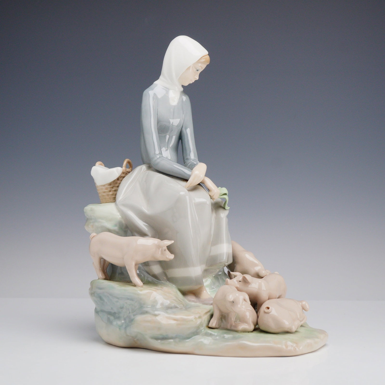 Lladro Porcelain Figurine Girl with Piglets 01004572: This Lladro porcelain figurine was designed by sculptor Fulgencio Garcia. The scene depicts a young farm girl in traditional dress, including a gray-blue bodice, a long gray skirt, and a white headsca