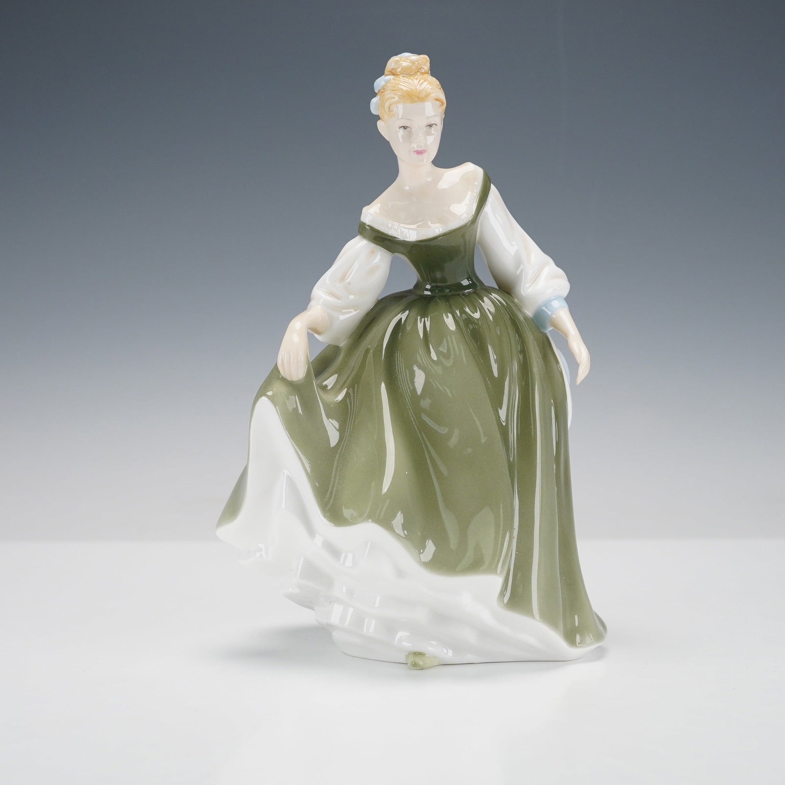 Royal Doulton Pretty Ladies Figurine, Fair Lady HN4719: A graceful lady in a flowing green gown with white accents and pale blue ribbons holds her skirt delicately as she steps forward. Her serene expression and refined pose capture timeless charm, finishe